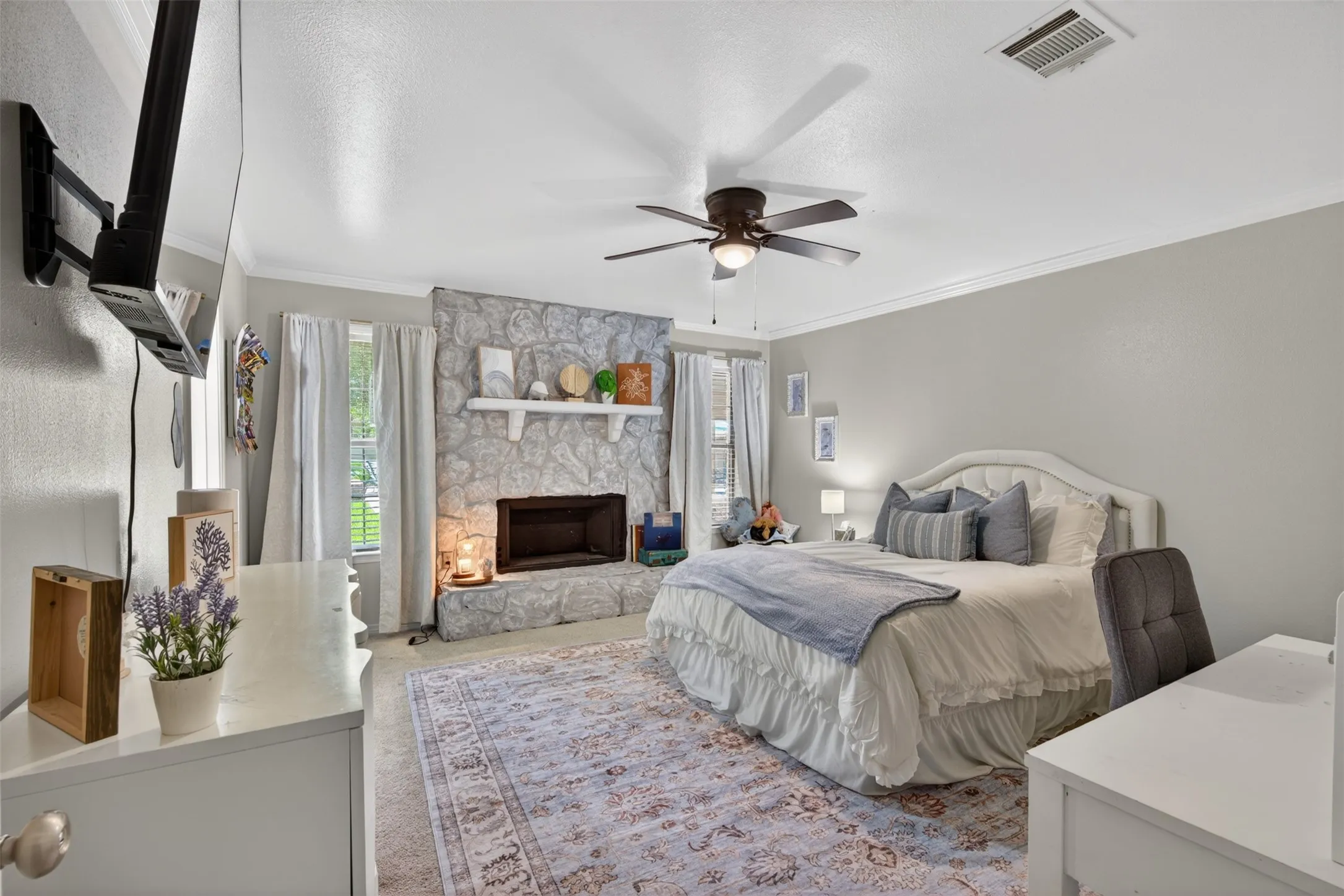 Stone-faced fireplace with a white mantel, ceiling fan with integrated lighting, recessed windows with trim, crown molding, and light-toned wall finishes