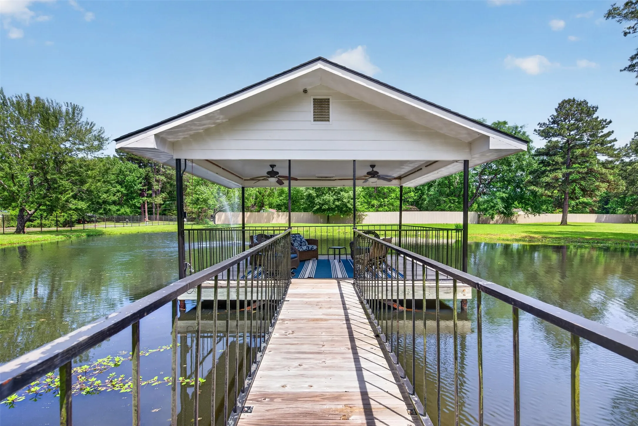 Covered dock structure featuring a wooden walkway, black metal railings, and a sheltered seating area