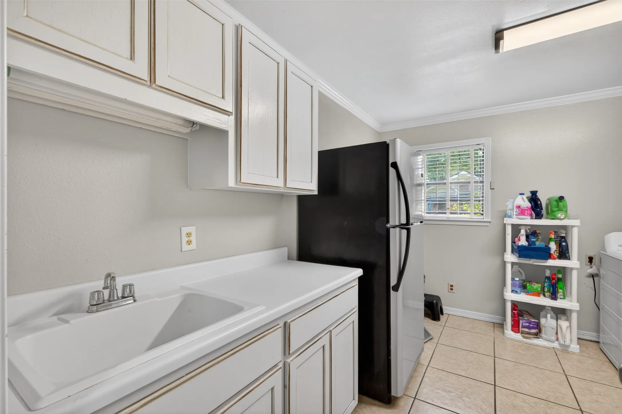 Utility room featuring a built-in sink with a chrome faucet, white cabinetry, and light-toned tile flooring