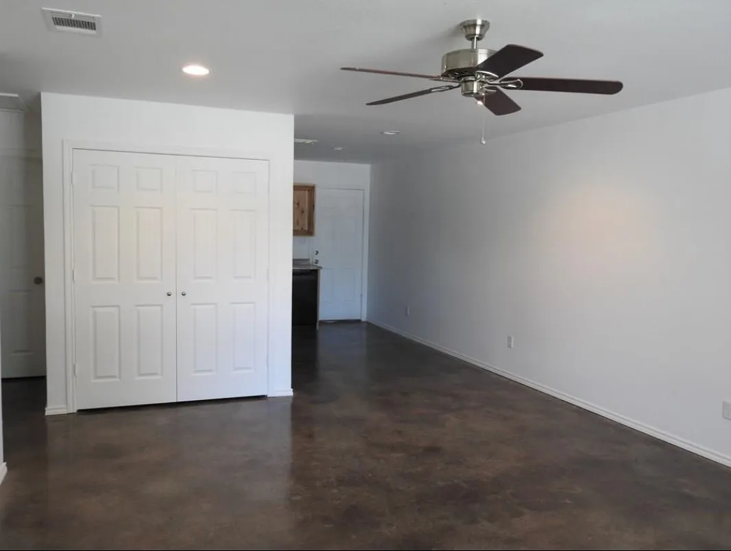 Spacious room featuring rich brown flooring, white walls, a ceiling fan with dark wood-finish blades, recessed lighting, and white bi-fold closet doors