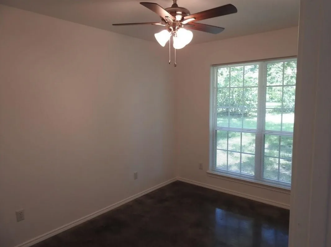 Room featuring a multi-pane window with blinds, a ceiling fan with integrated lighting, neutral wall paint, and dark-toned flooring