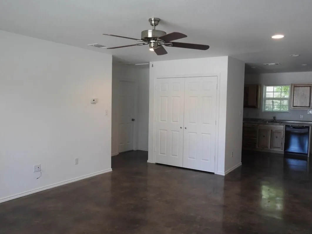 Spacious living area featuring polished concrete flooring, recessed lighting, a ceiling fan, bi-fold closet doors, and access to a kitchen with a window