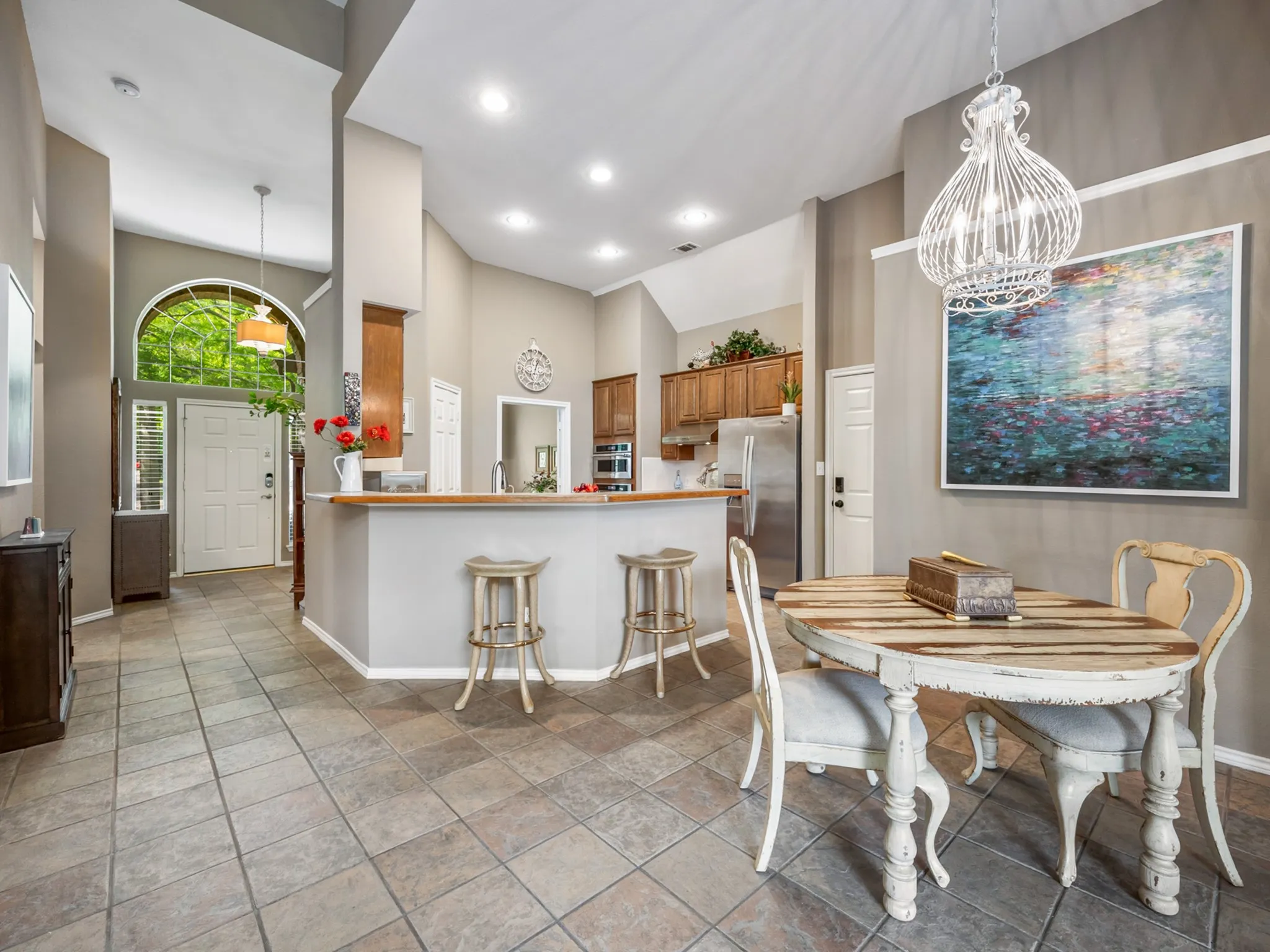 Spacious open-concept living area featuring tile flooring, vaulted ceilings, recessed lighting, and a breakfast bar with a wood-finish countertop