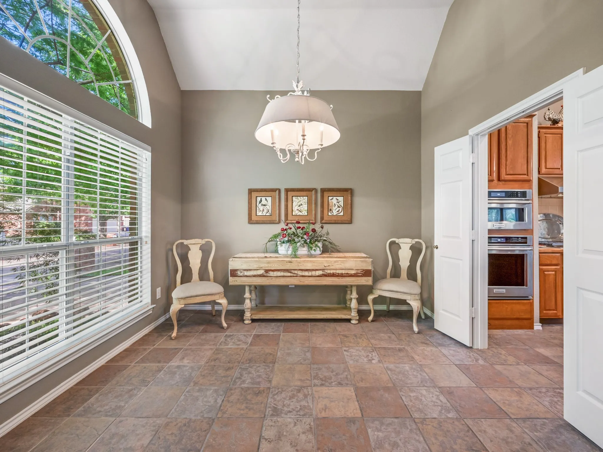 Vaulted ceiling room featuring tiled flooring, a large arched-top window, and double doors opening to a kitchen with built-in appliances and wood cabinetry