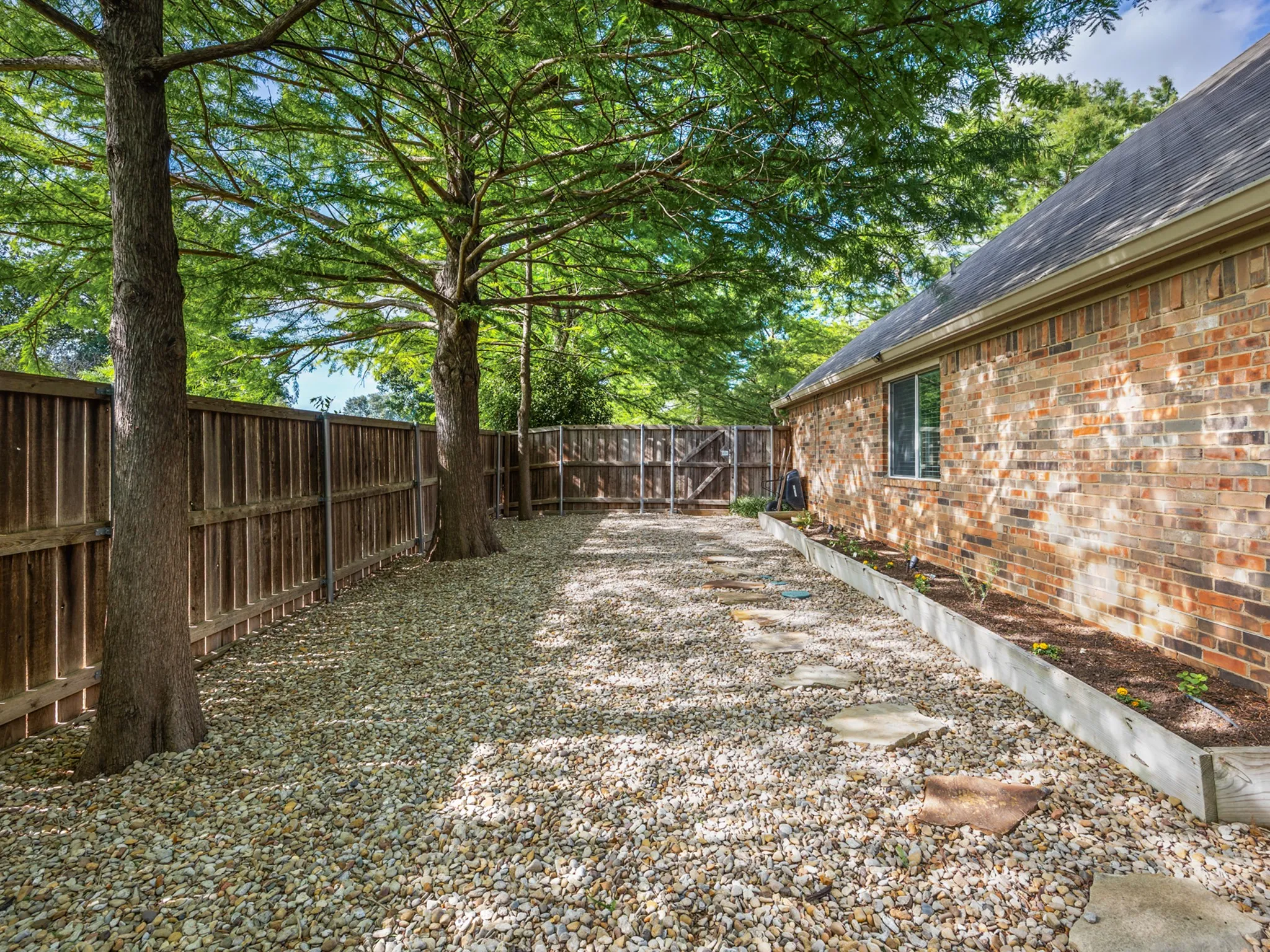 Side yard featuring a full privacy fence, mature trees, and a gravel ground cover