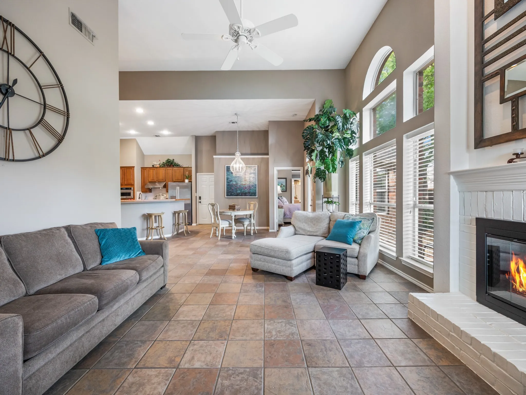 Expansive living area featuring high vaulted ceilings, multi-toned tile flooring, and a white brick fireplace with a dark insert