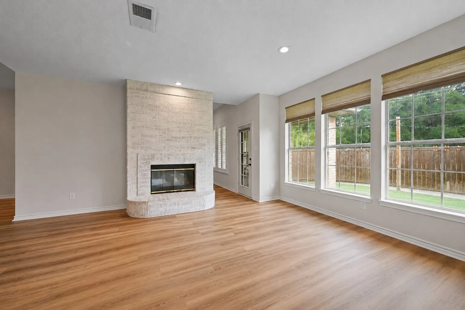 Spacious room with wood-finish flooring, a textured stone-finish fireplace, and recessed lighting