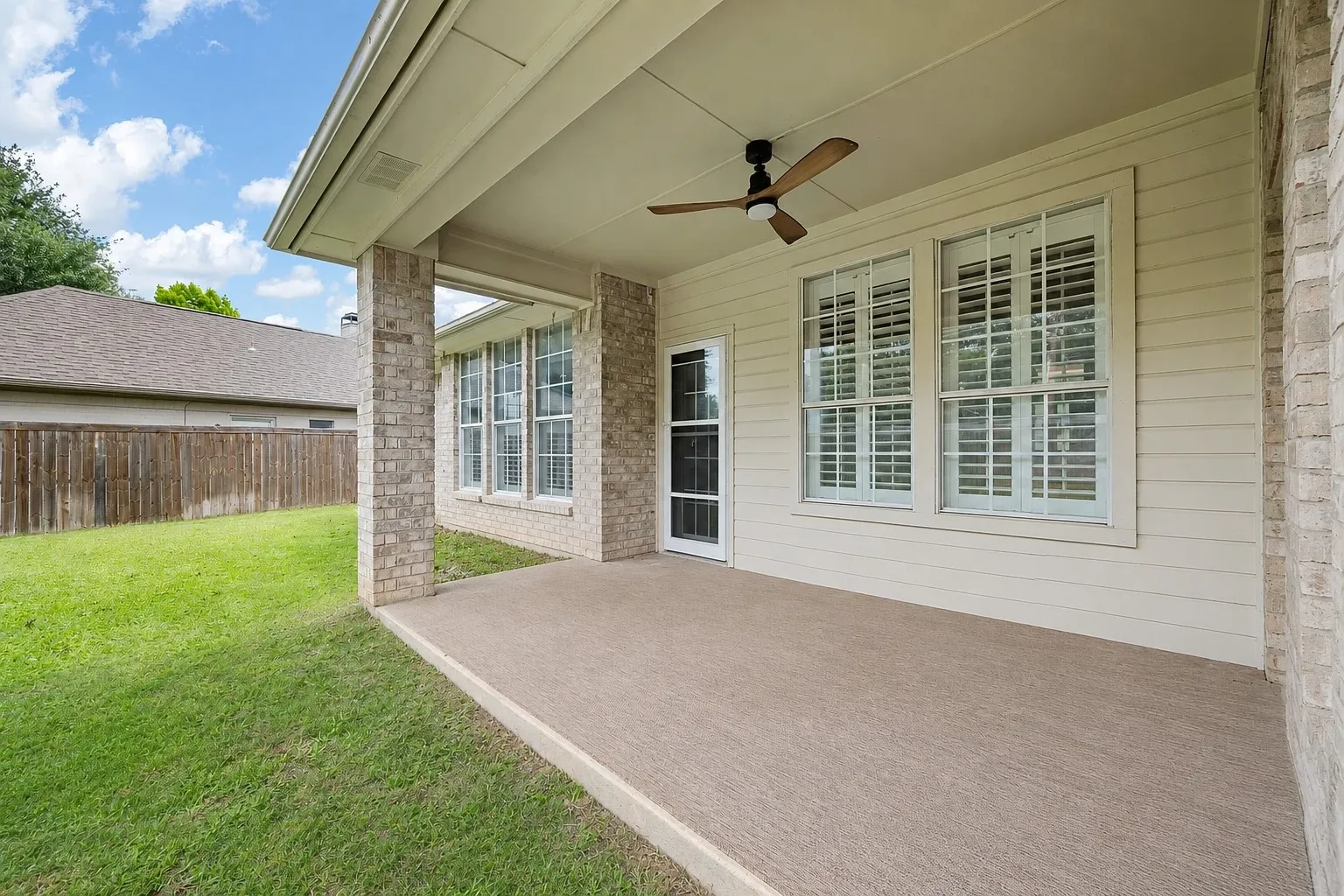 Covered patio with a ceiling fan, light brick columns, and a textured concrete surface