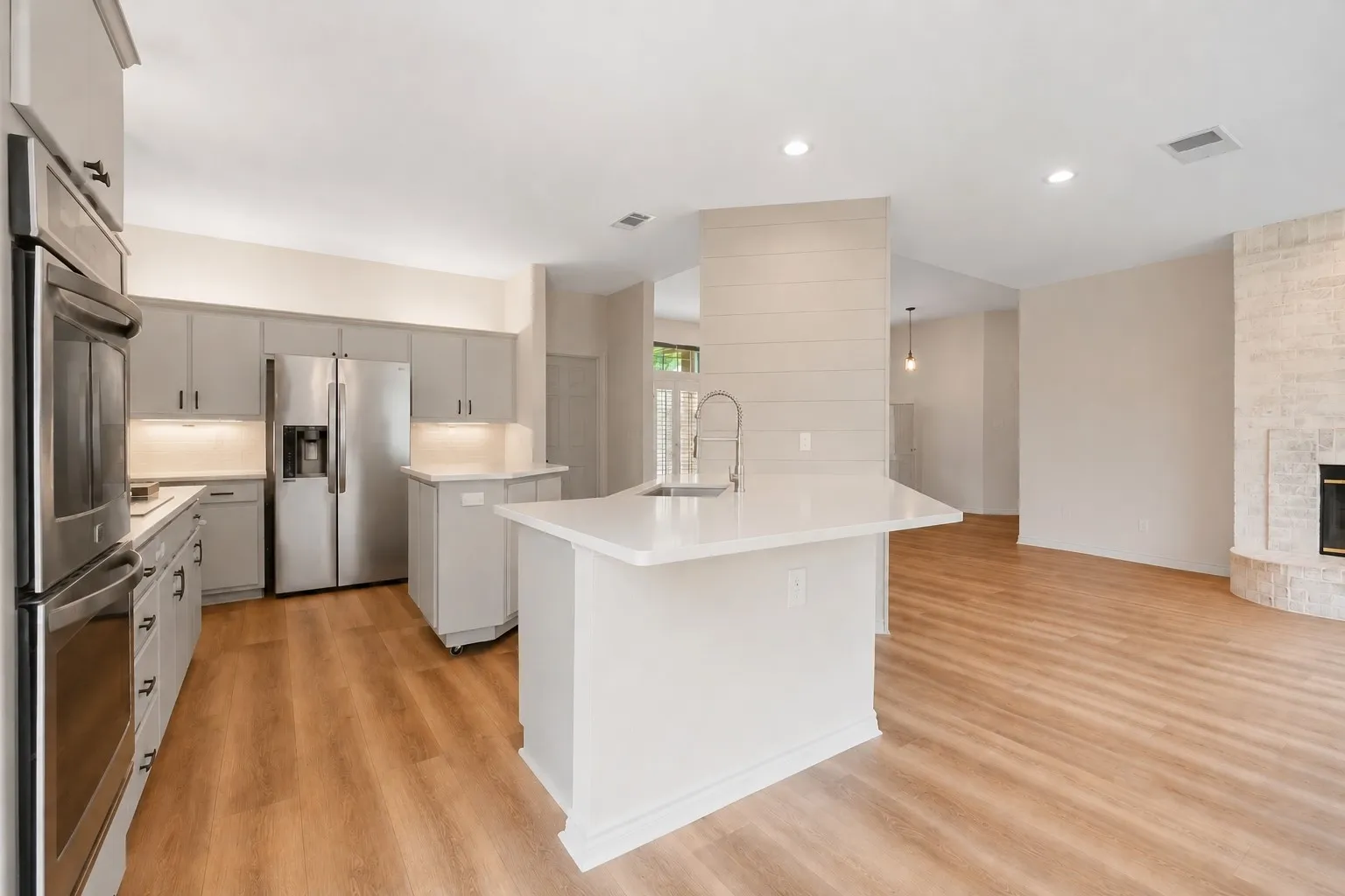 Open-concept kitchen featuring an island with a breakfast bar, light wood-finish flooring, recessed lighting, stainless steel appliances, and grey cabinetry with under-cabinet lighting