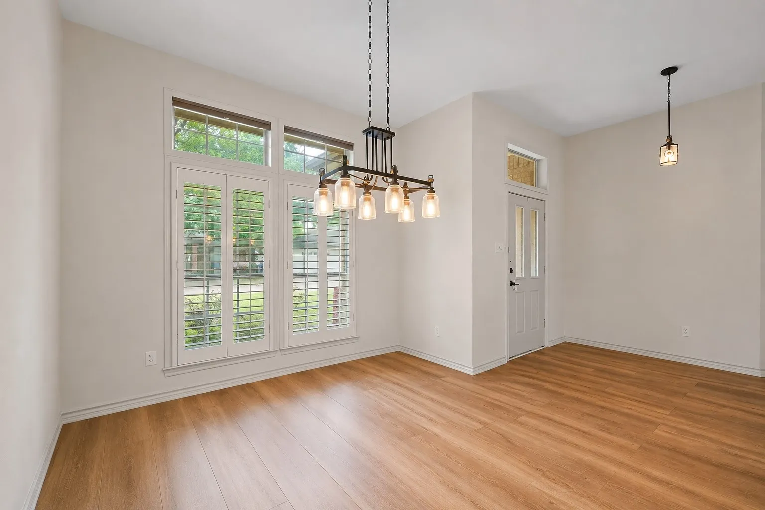 Dining area featuring wood-finish flooring, a multi-pane glass entry door with transom window, and a chandelier with glass shades