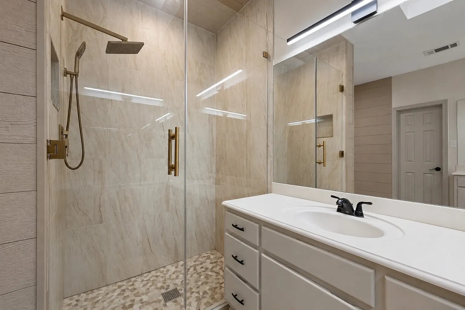Enclosed shower with a frameless glass door, gold-finish fixtures, and a tiled shower niche