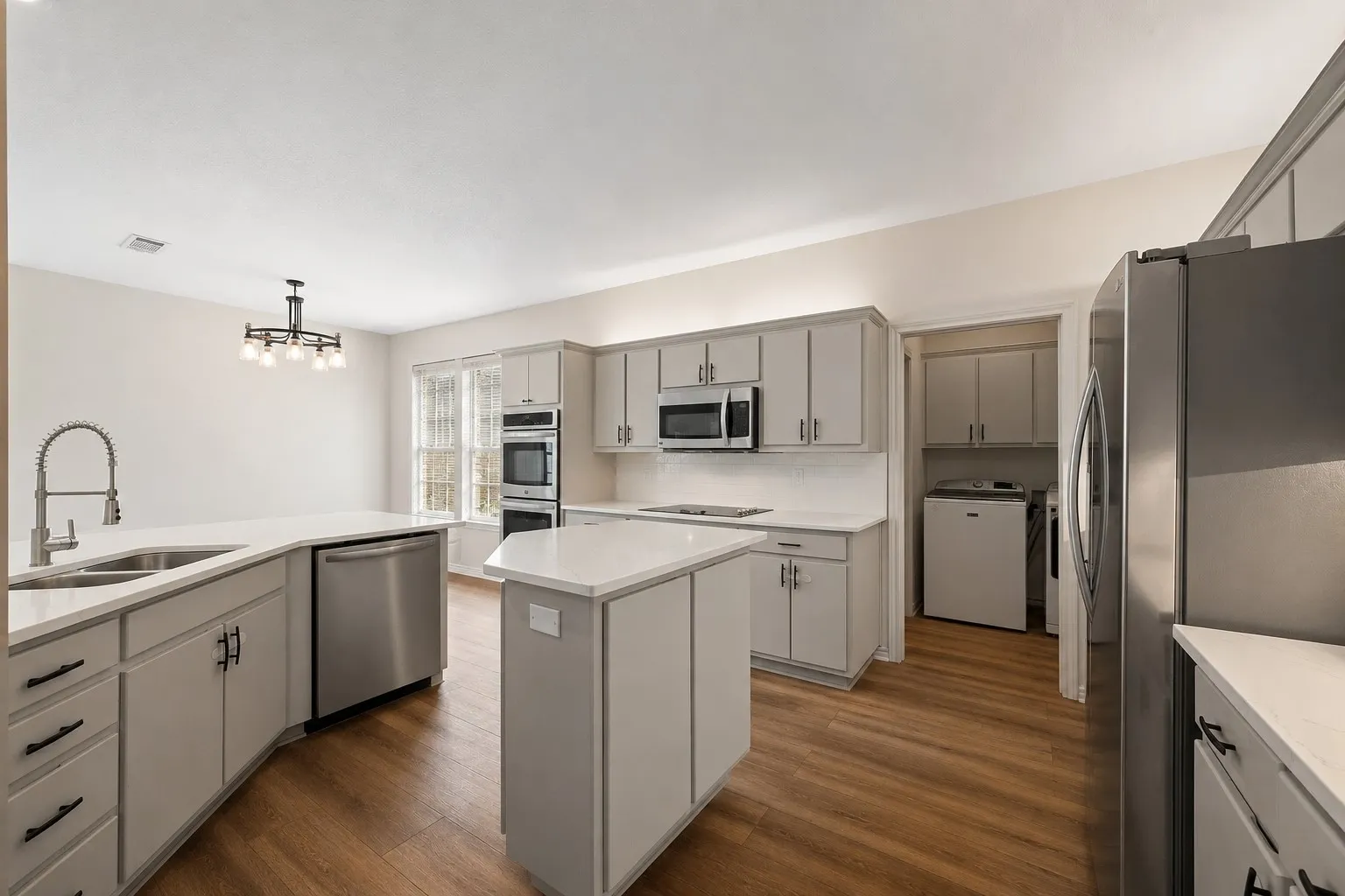 Kitchen featuring wood-finish flooring, light grey cabinetry, stainless steel appliances, white countertops, and a central island
