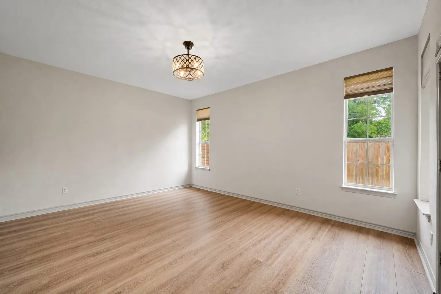 Spacious Primary Bedroom featuring wood-finish flooring, light neutral wall paint, and two windows with natural light and woven shades
