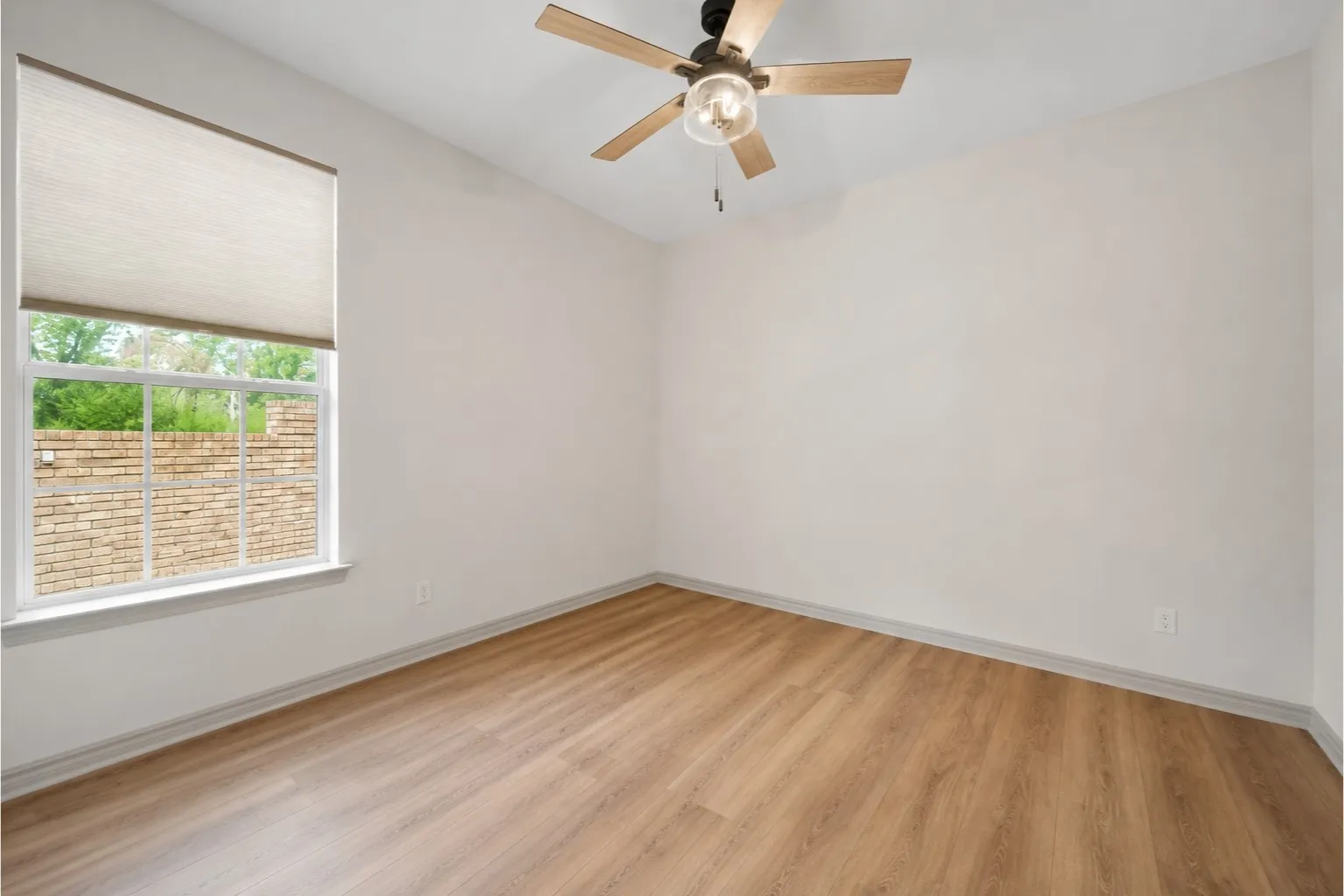 Room featuring wood-finish flooring, a contemporary ceiling fan, and a double-paned window with a roller shade