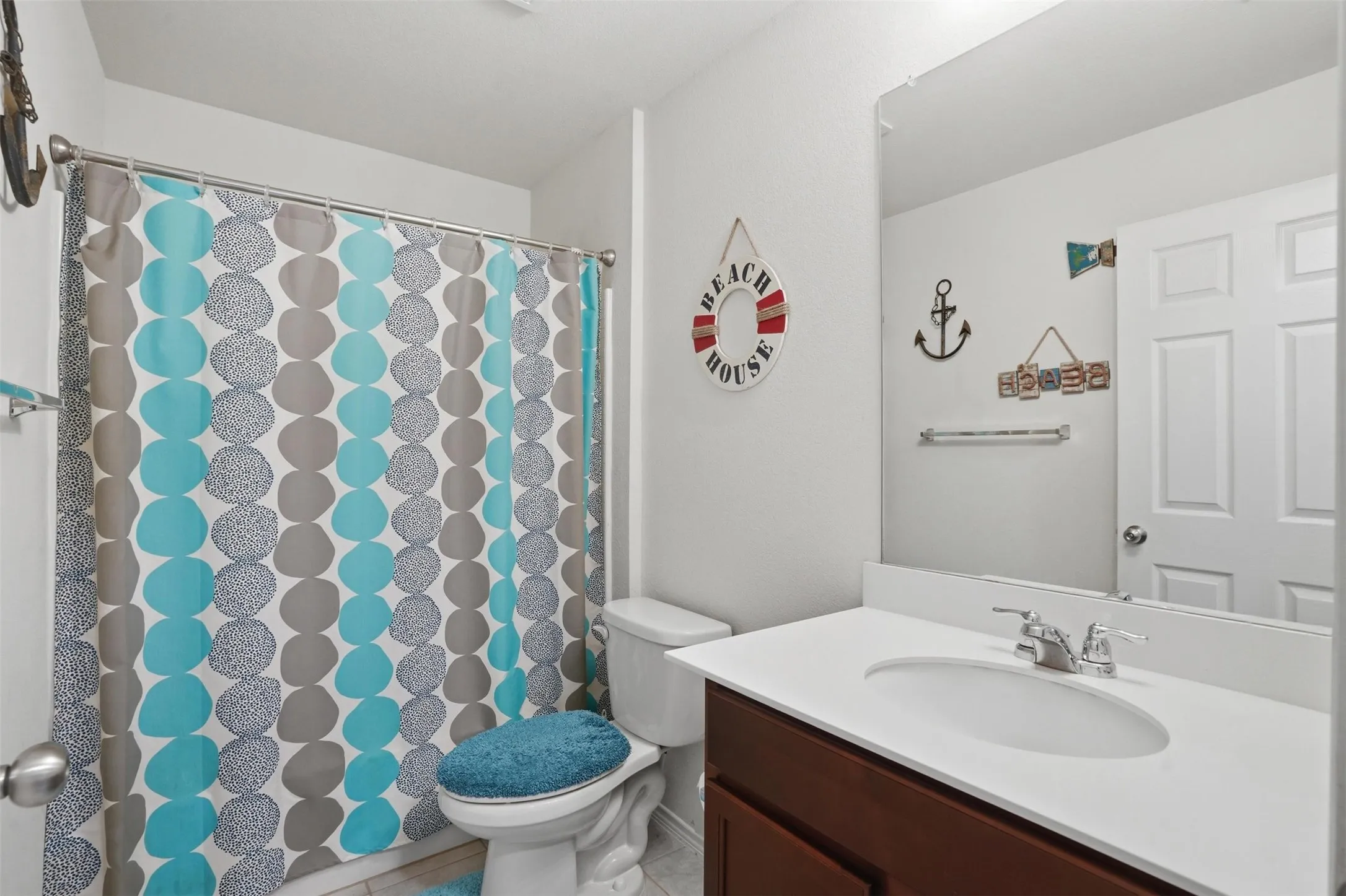 Bathroom featuring a vanity with a white countertop and an integrated sink, a large wall-mounted mirror, a toilet, and a shower with a chrome shower rod
