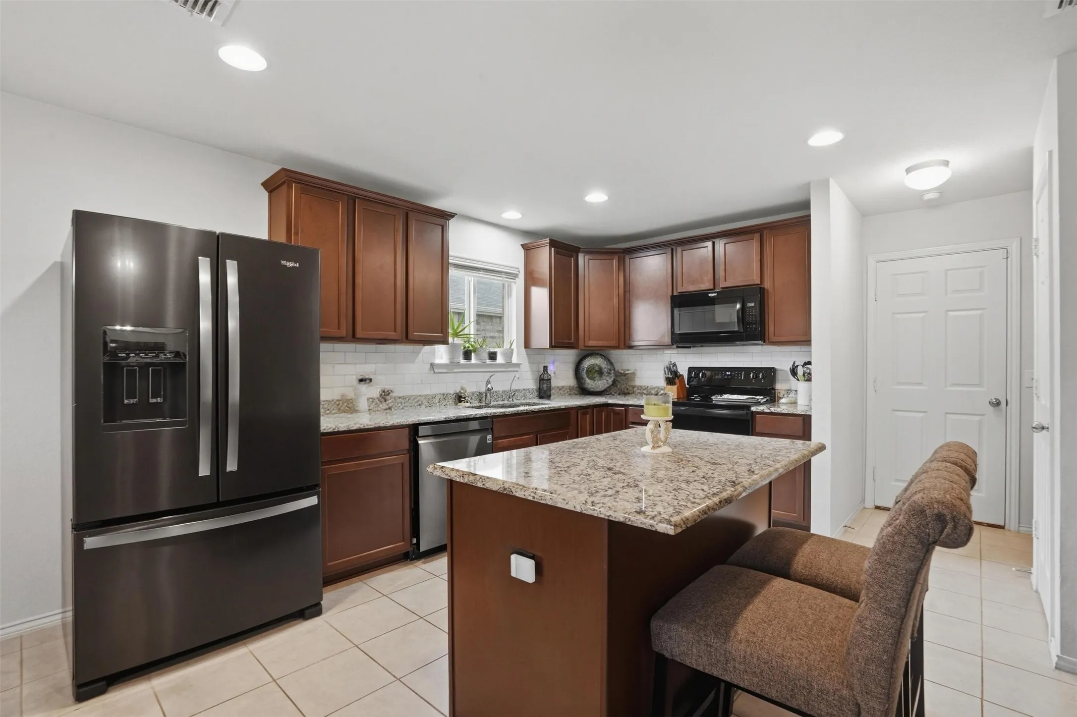 Kitchen featuring a central island with a granite-style countertop, dark wood cabinetry, a subway tile backsplash, recessed lighting, and tile flooring