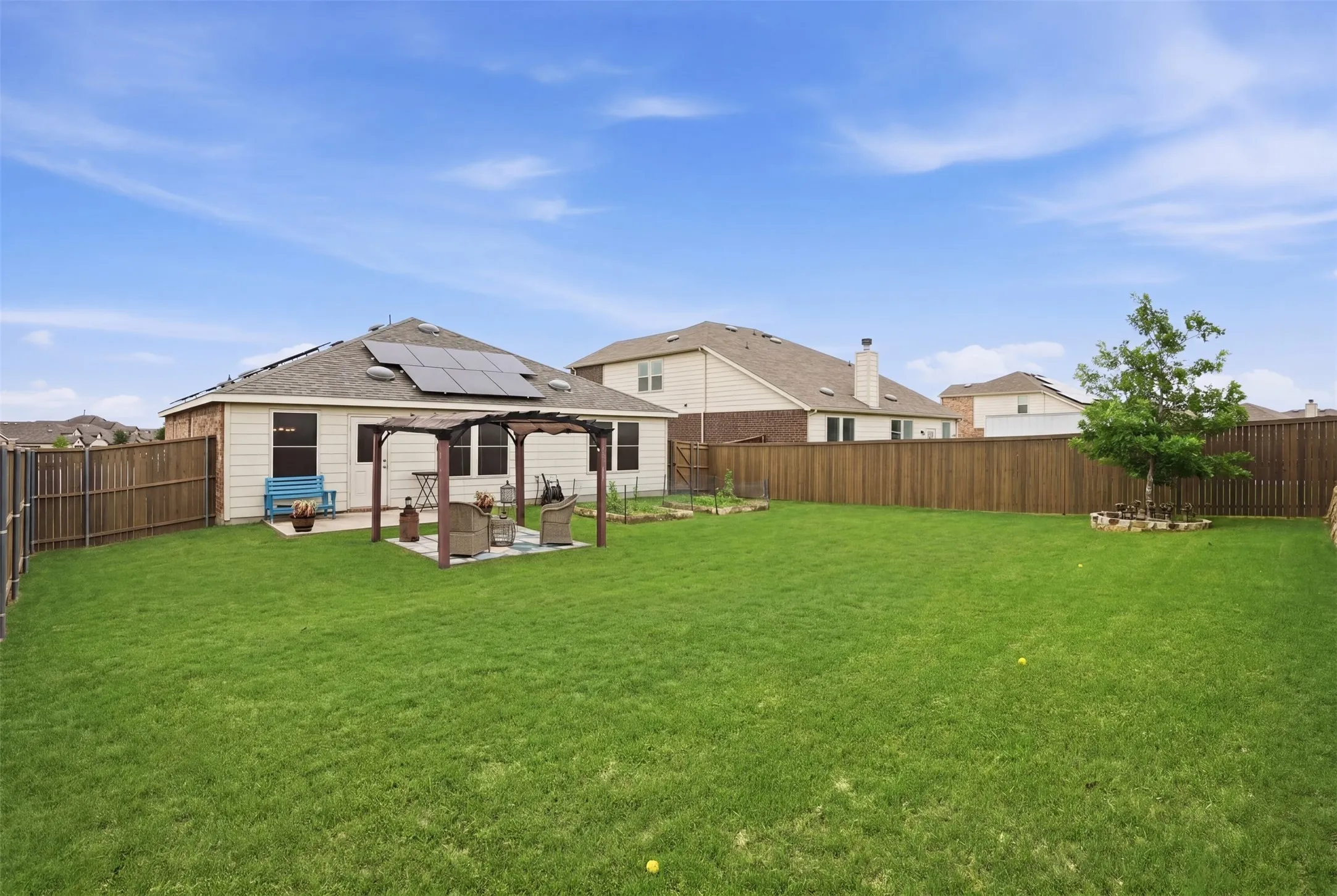 Expansive fenced backyard featuring a large green lawn, a privacy fence, and a patio with a pergola