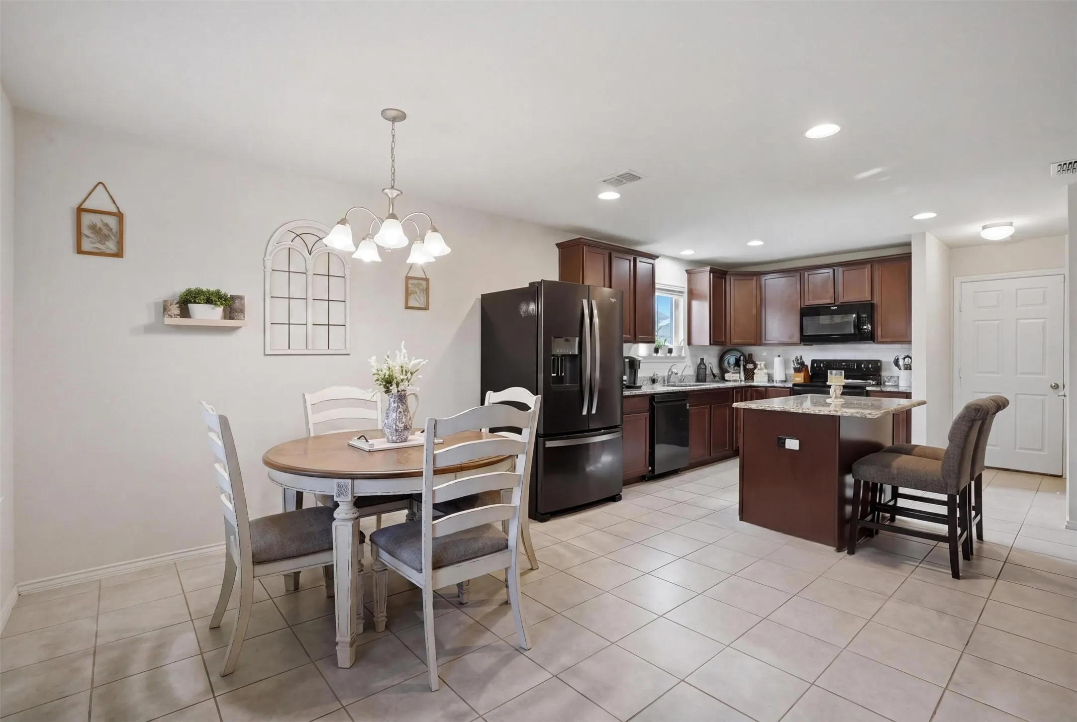 Open-concept kitchen and dining area featuring tile flooring, dark wood cabinetry, a central island with a light-toned countertop, and recessed lighting