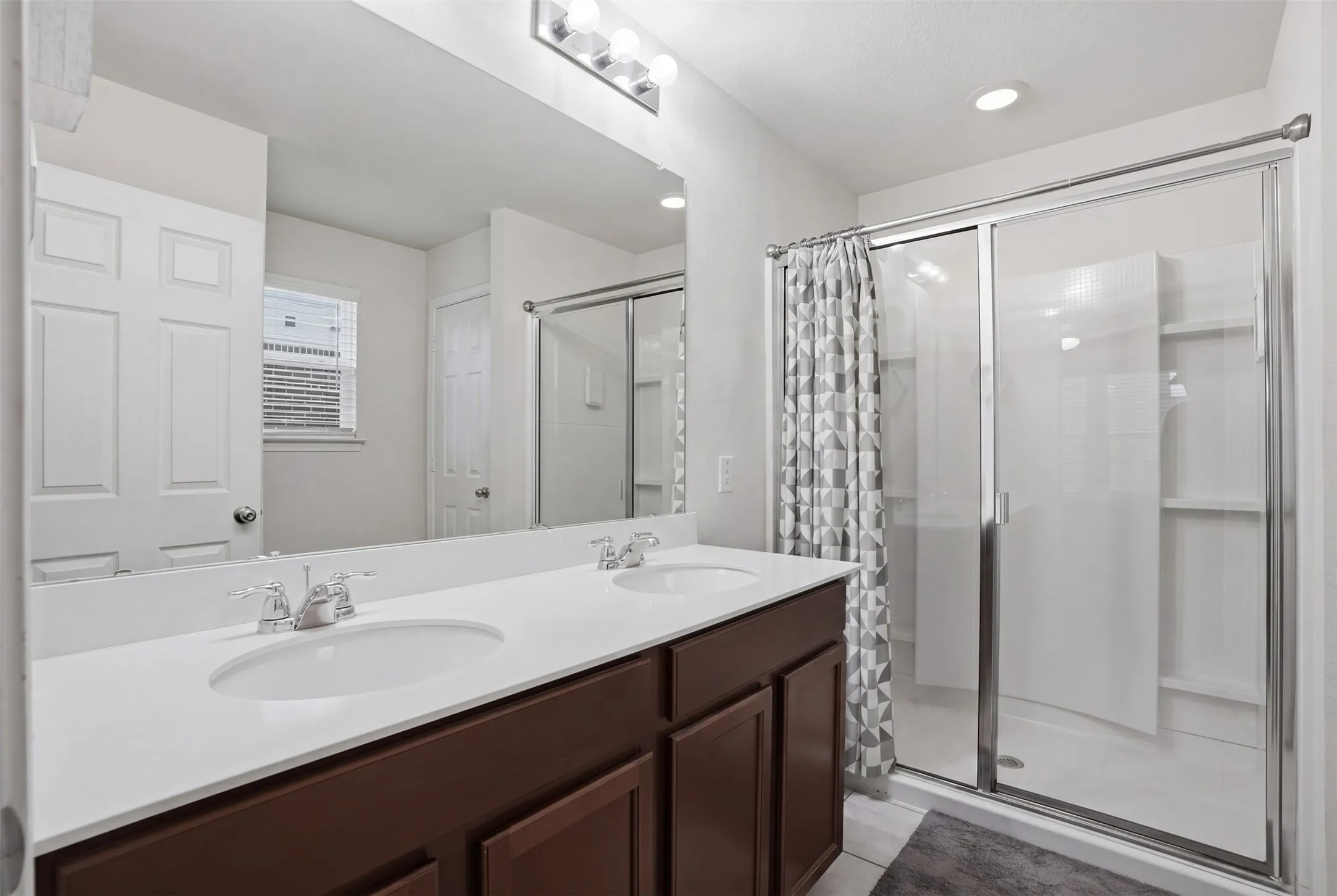 Bathroom featuring a double vanity with white countertops, dual undermount sinks, and a framed glass shower enclosure
