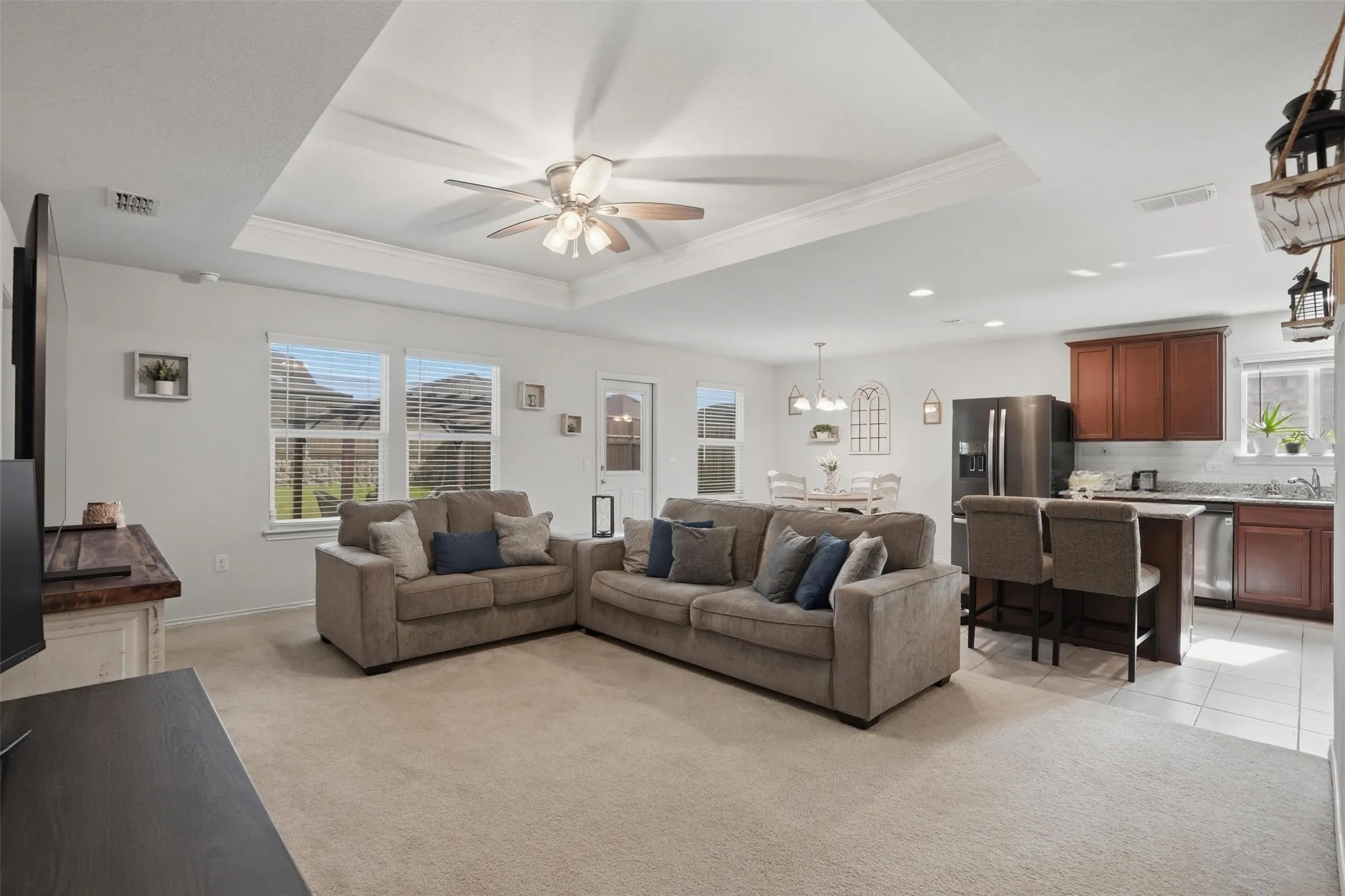 Open-concept living area with tray ceiling, ceiling fan, and carpet flooring