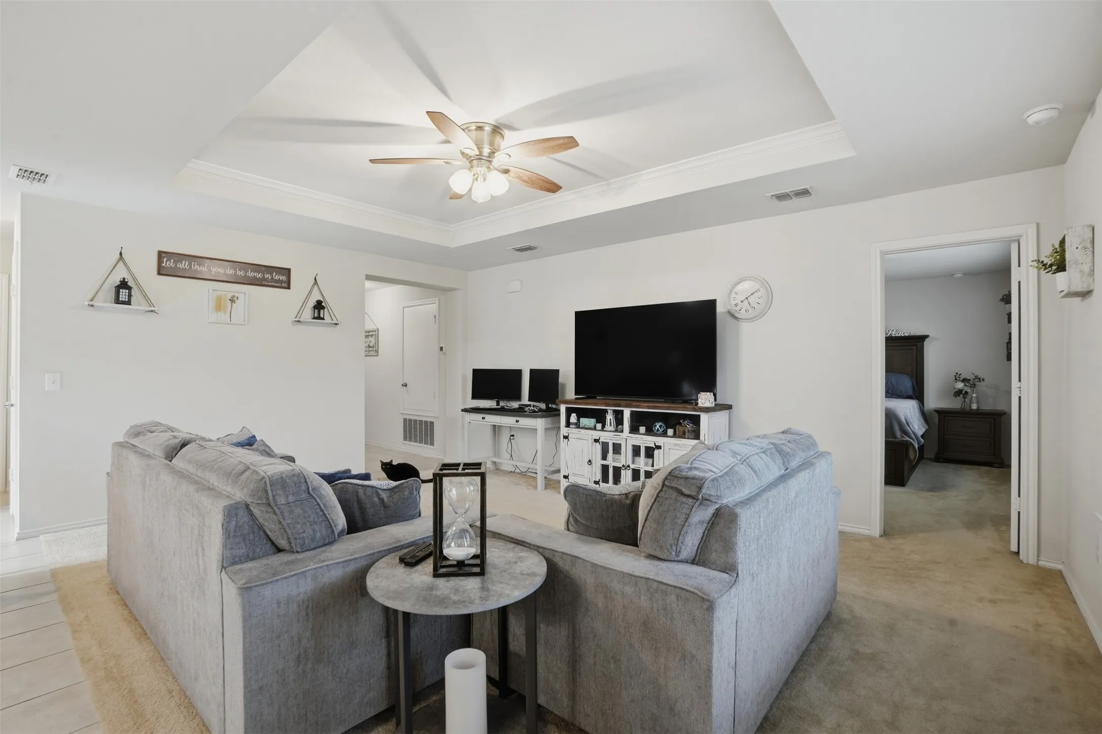 Living area featuring a tray ceiling with crown molding, ceiling fan, and carpet flooring