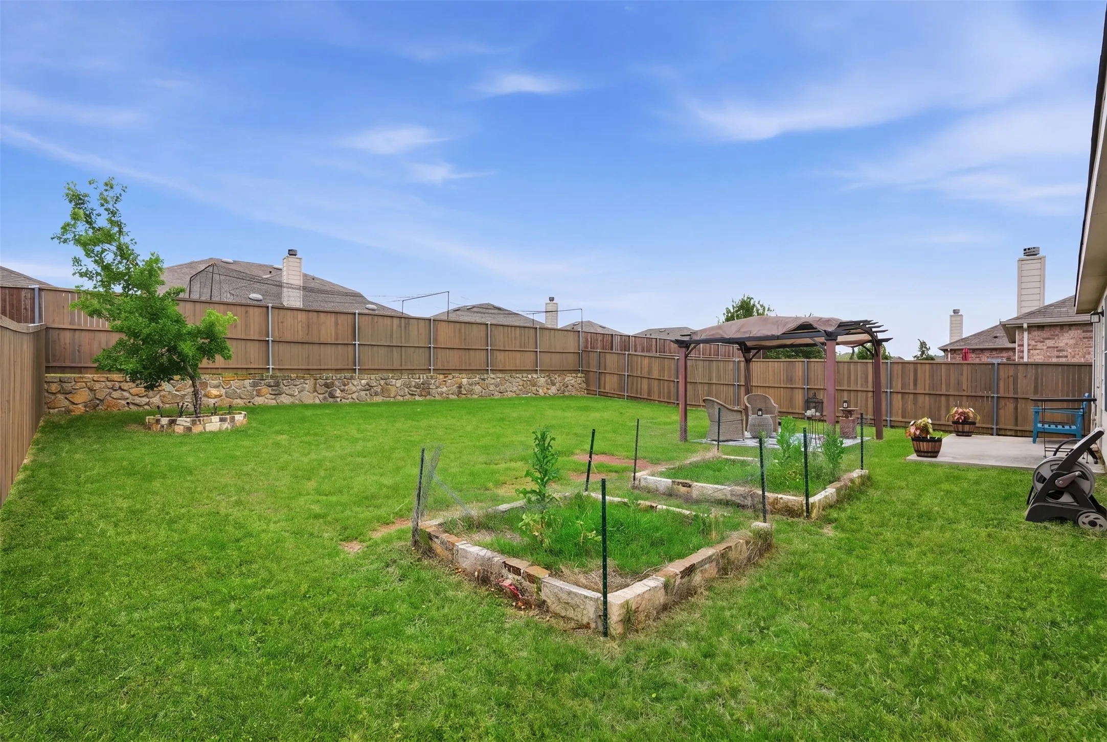 Expansive backyard featuring a lush green lawn, full privacy fencing, and a retaining wall