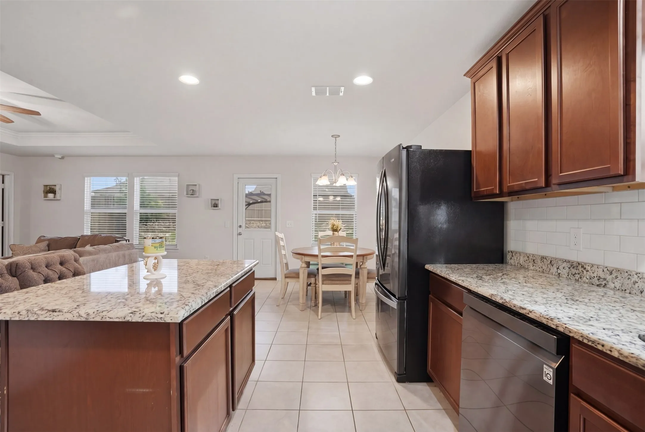 Kitchen featuring granite countertops, wood cabinetry, stainless steel dishwasher, and a tile backsplash