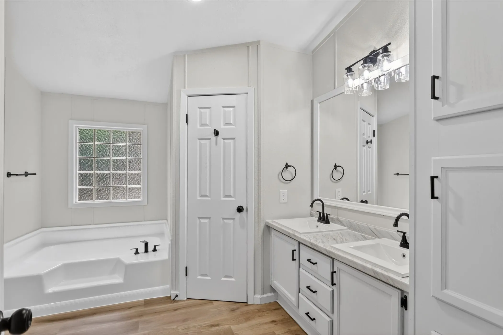 Dual sink vanity with white cabinetry, black hardware, and an expansive mirror