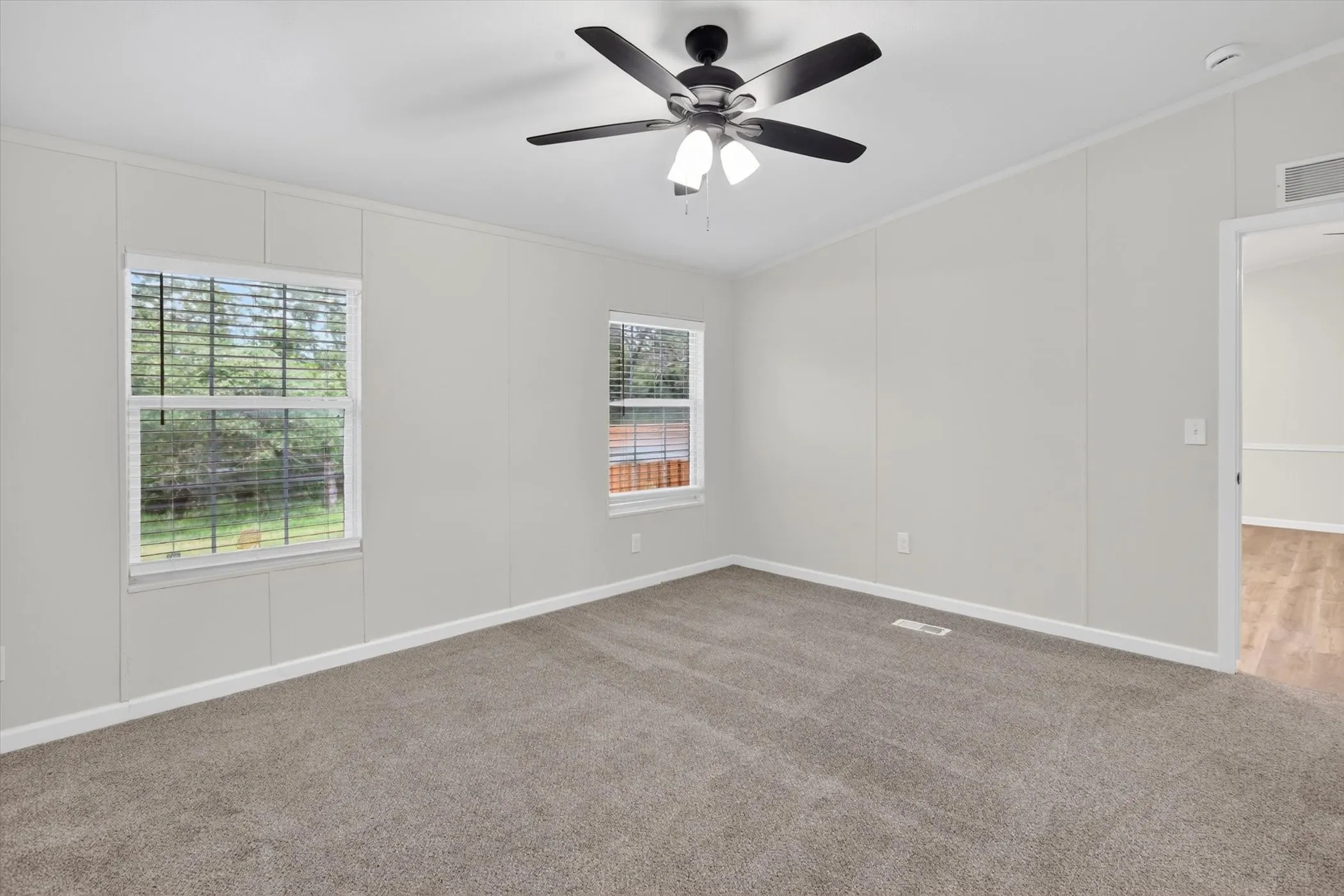 Carpeted room featuring light gray walls, white trim, two windows with blinds, and a ceiling fan with integrated lighting