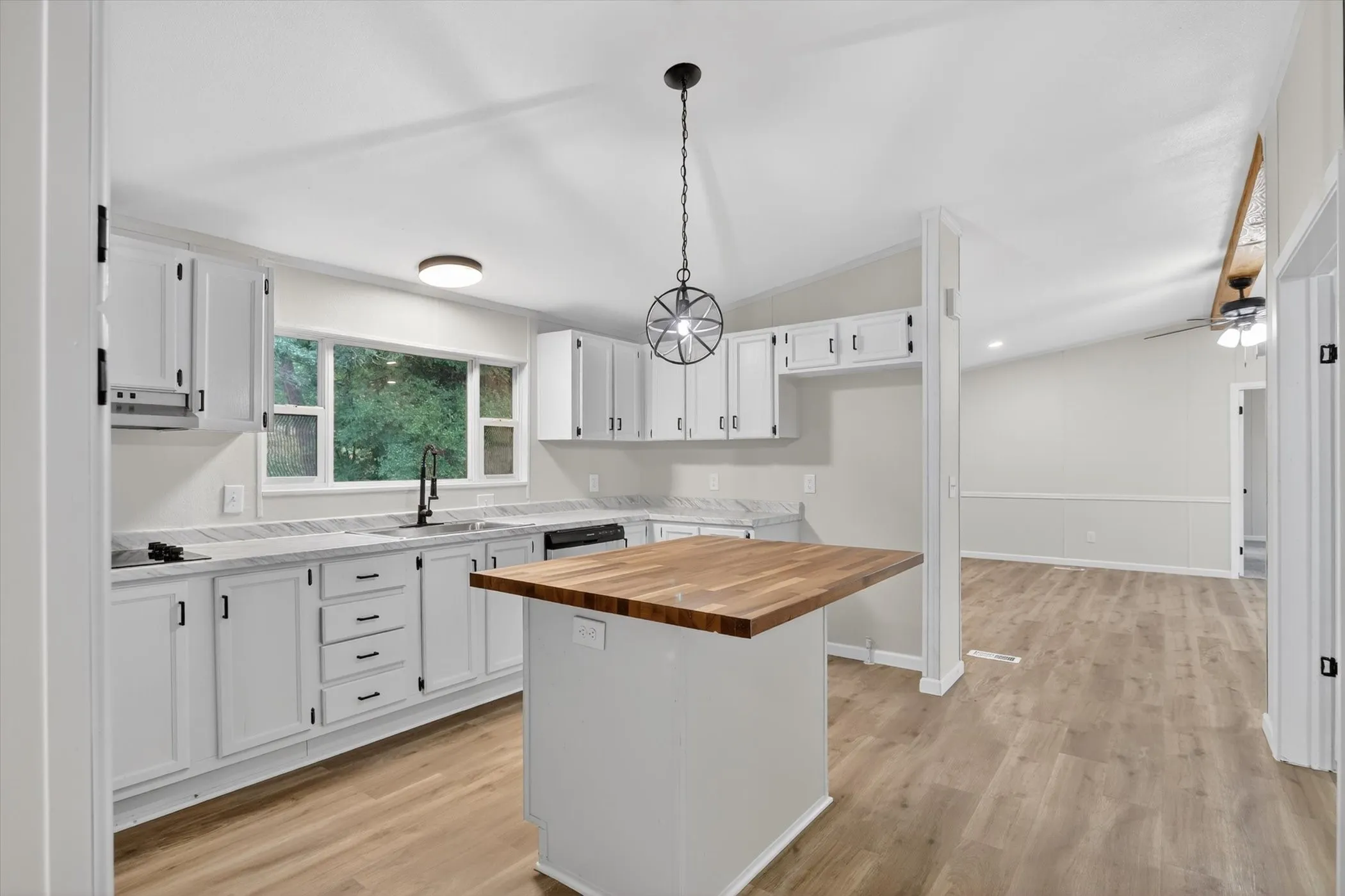 Open-concept kitchen featuring white cabinetry, light-toned wood-finish flooring, and a central island with a wood countertop