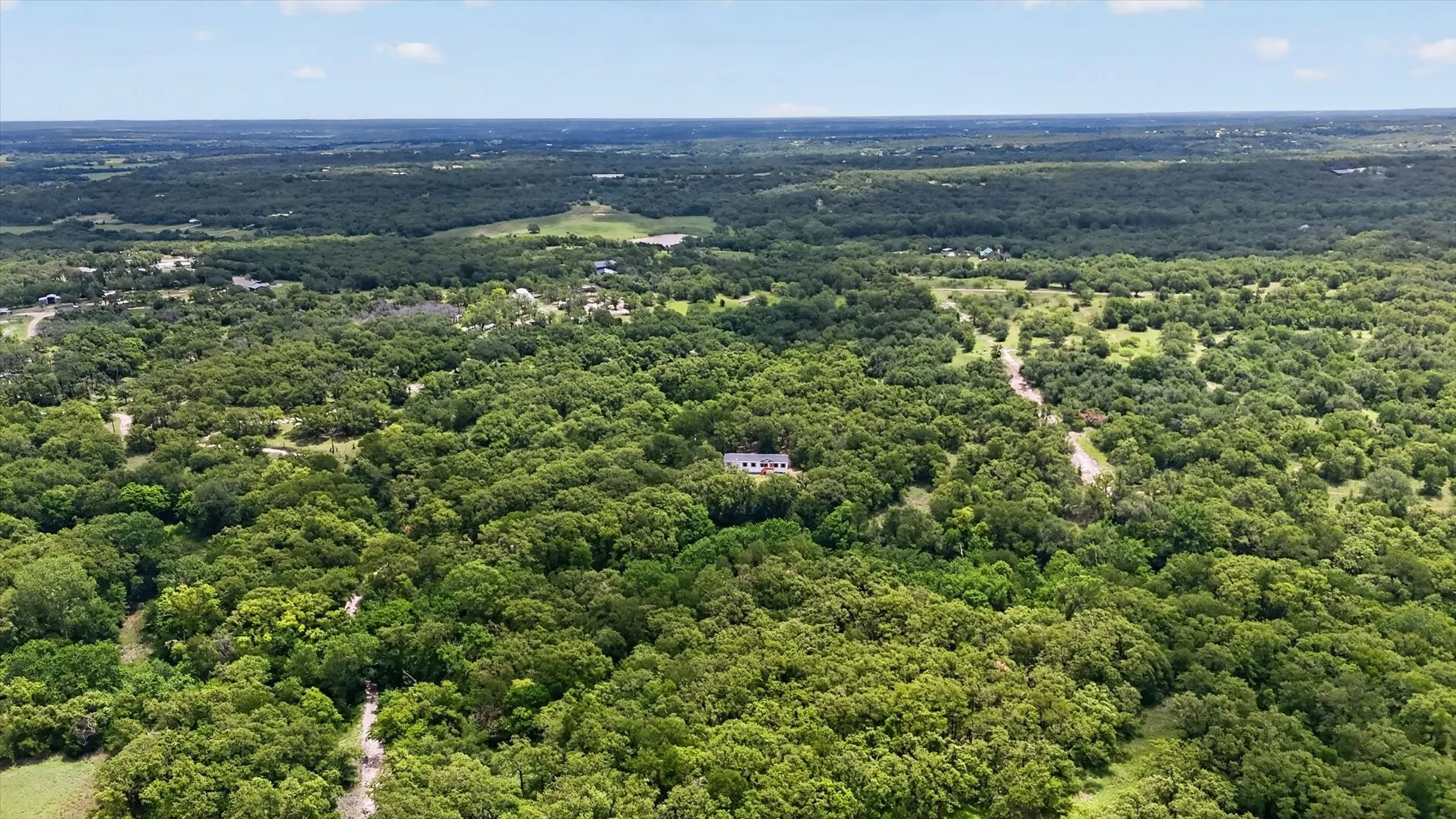 Expansive wooded acreage featuring a single-story residence with a light-colored exterior and dark roof, surrounded by mature trees