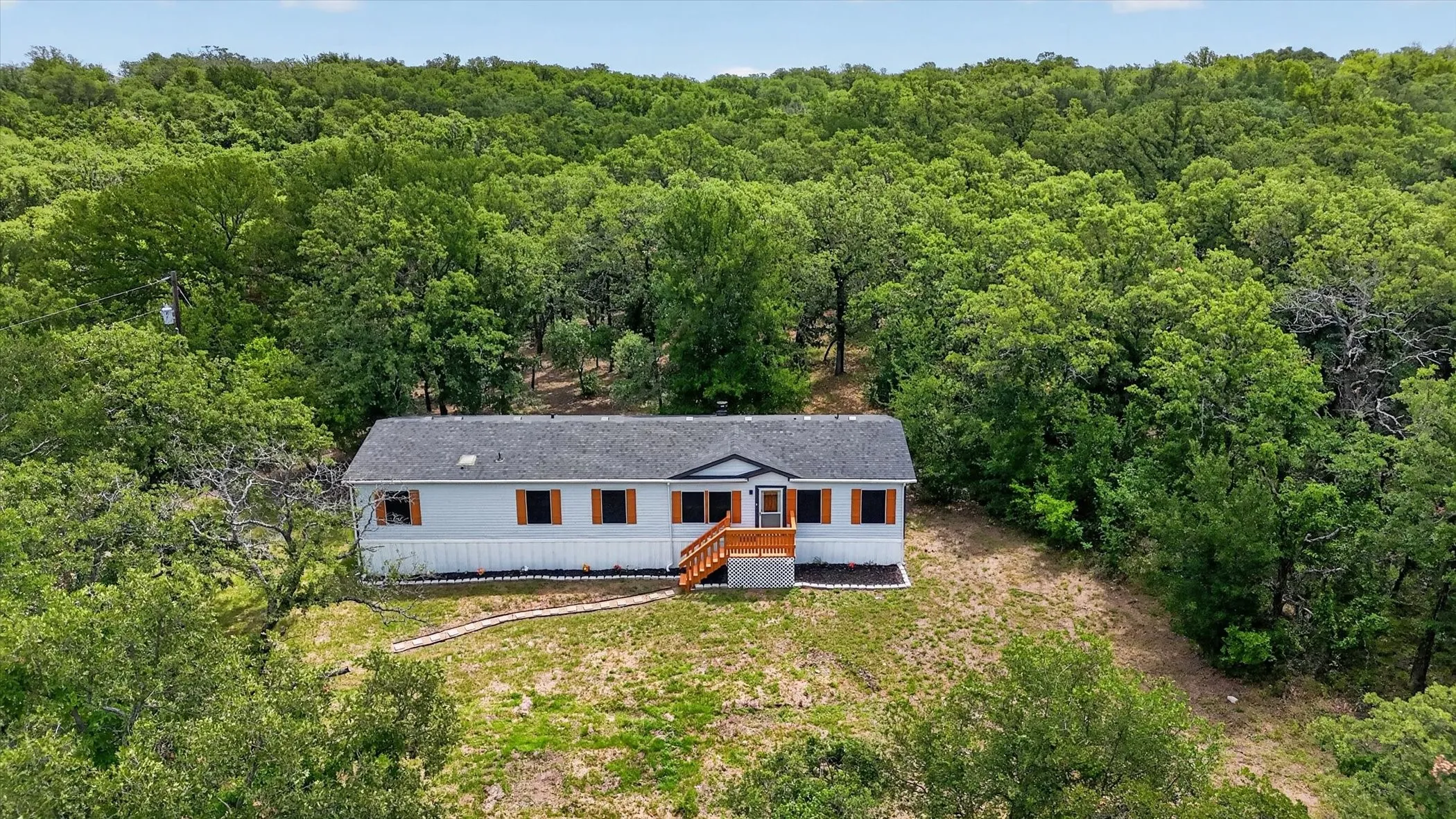 Spacious property featuring a single-story residence with light gray siding, dark roof, and wood-finish shutters