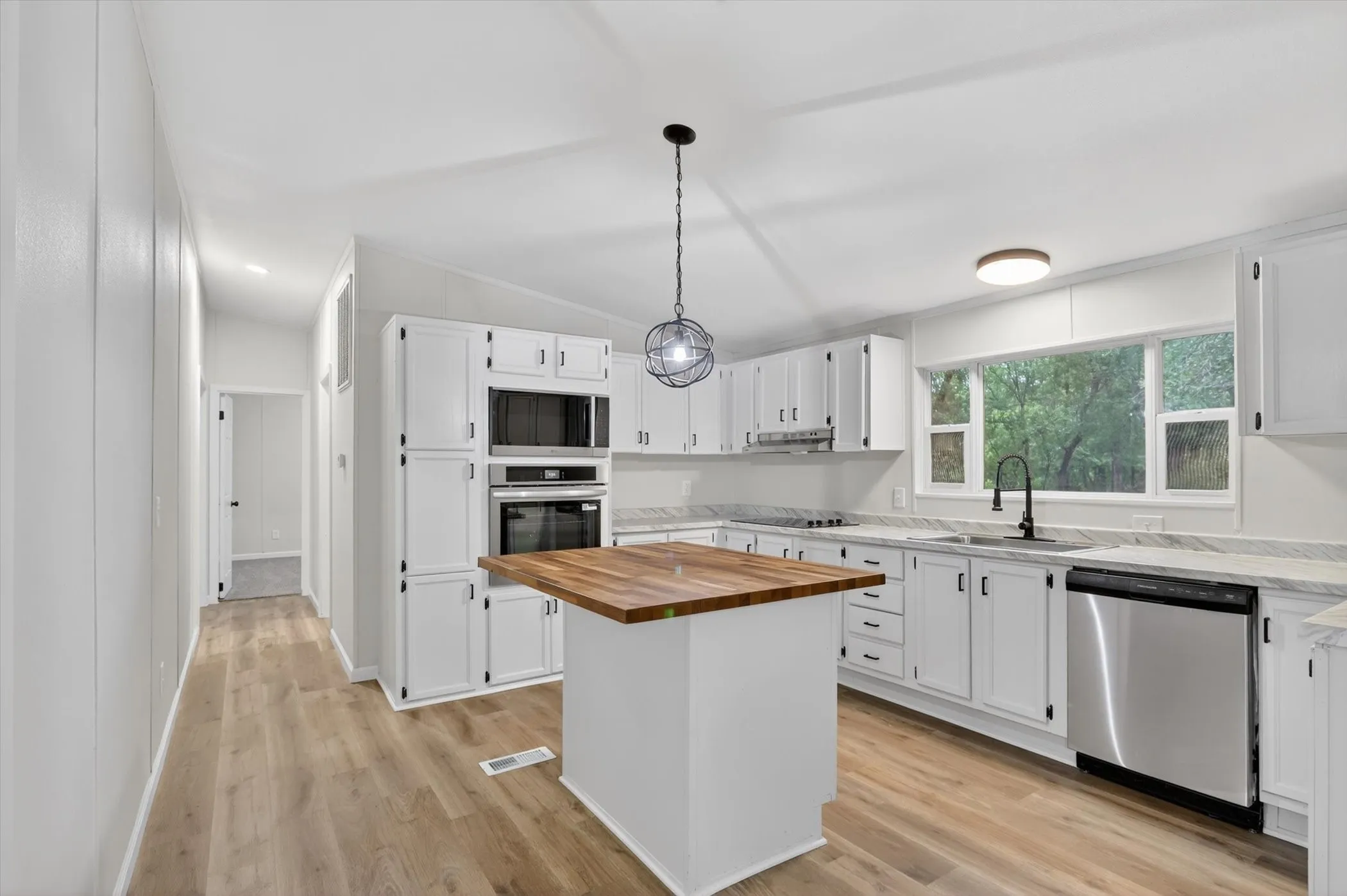 Bright kitchen featuring a central island with a wood-finish countertop, white cabinetry with dark hardware, built-in stainless steel appliances, and wood-finish flooring