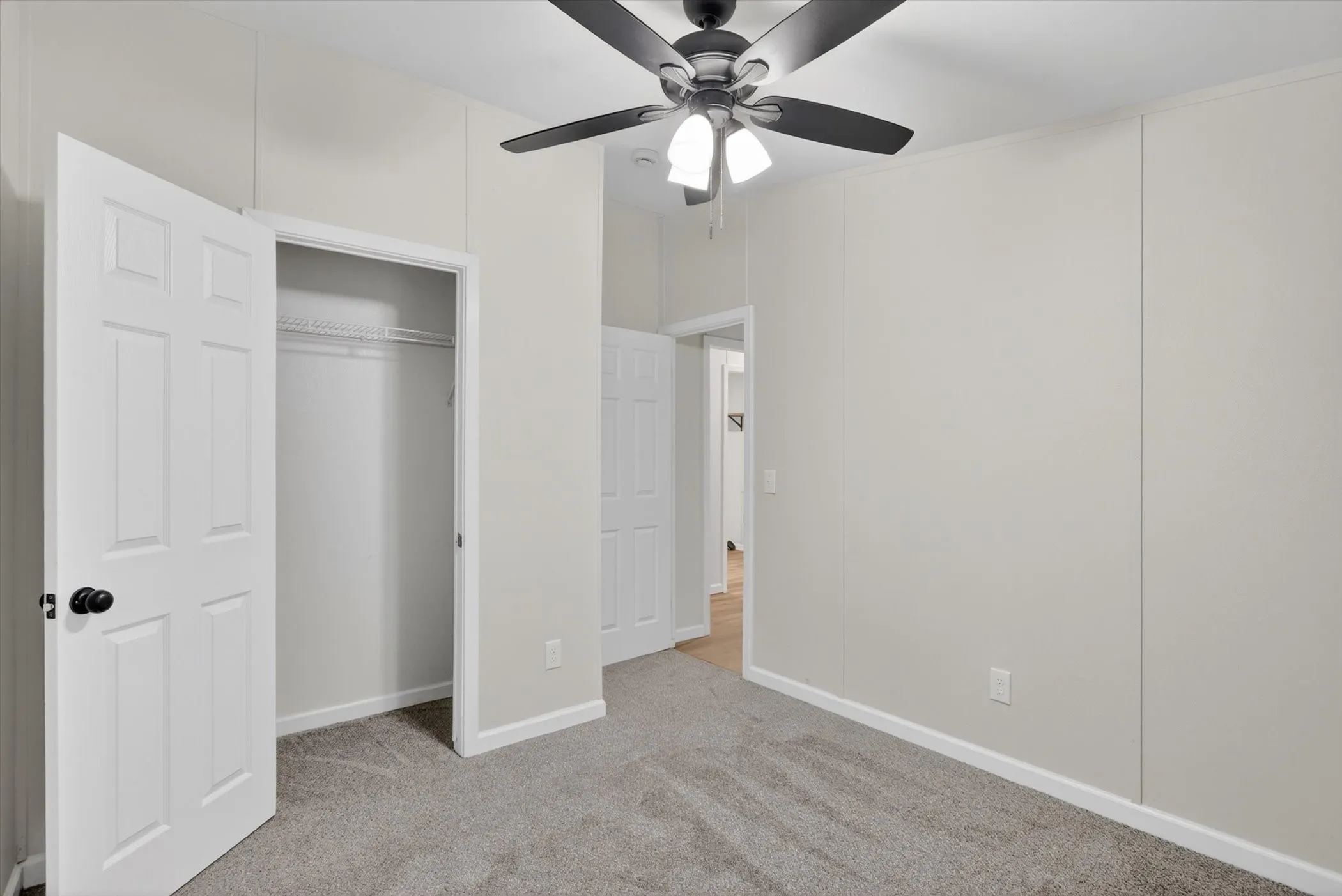 Carpeted room featuring a ceiling fan with integrated lighting, a paneled interior door, and a built-in closet with wire shelving