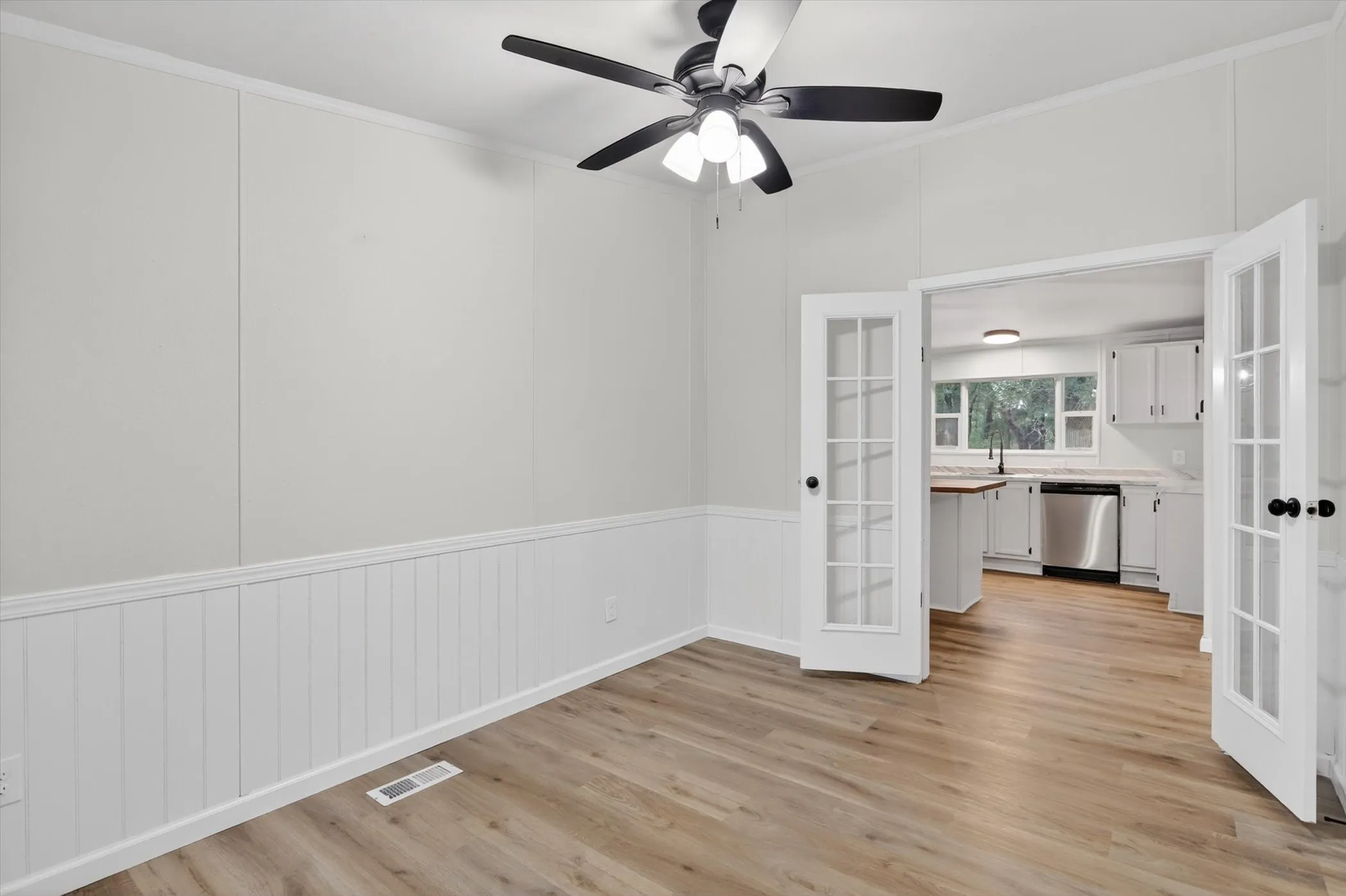 Spacious room featuring wood-finish flooring, white wainscoting, and a ceiling fan with integrated lighting