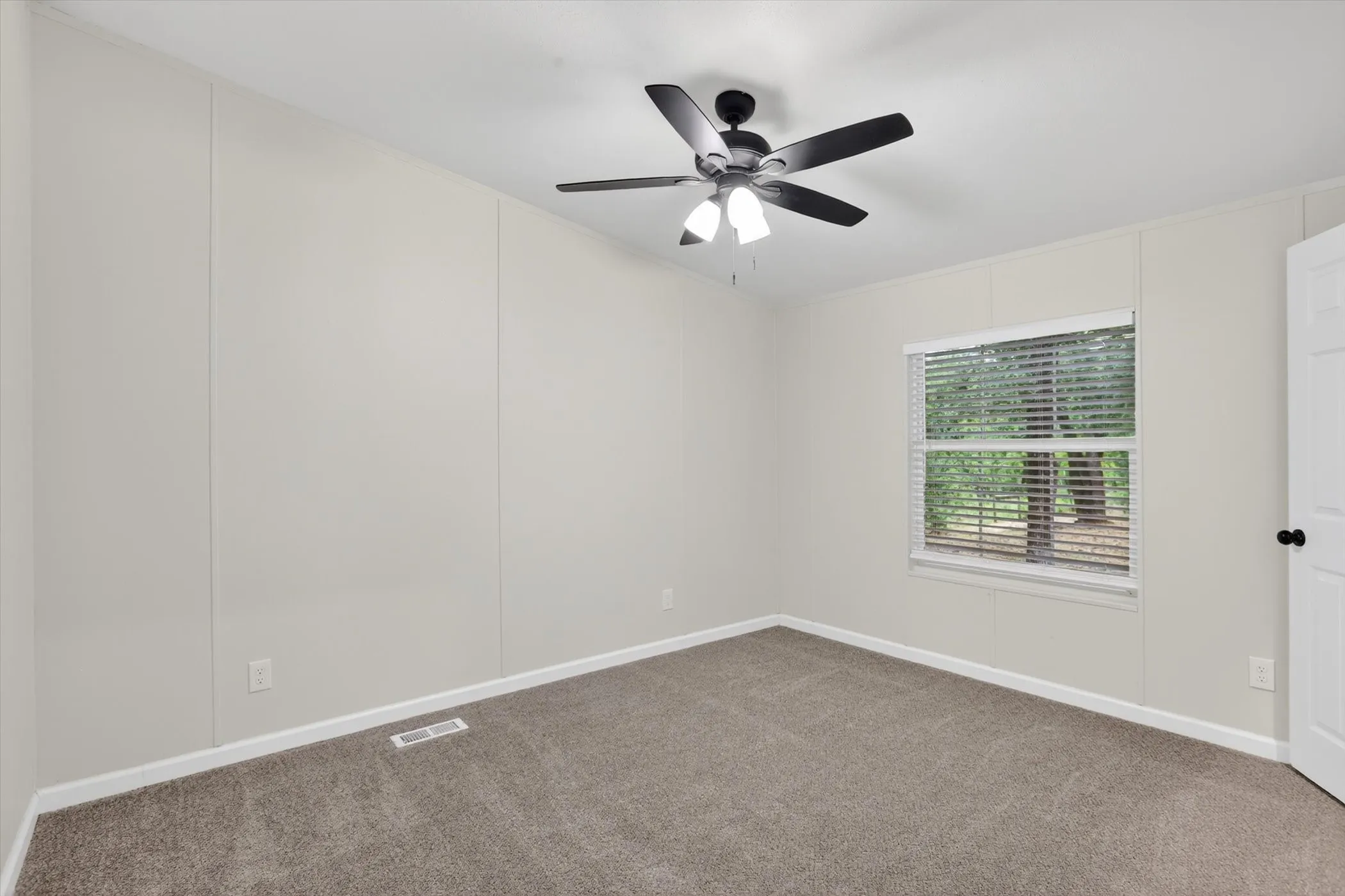 Spacious room featuring neutral carpeting, light-toned paneled walls, and a white ceiling