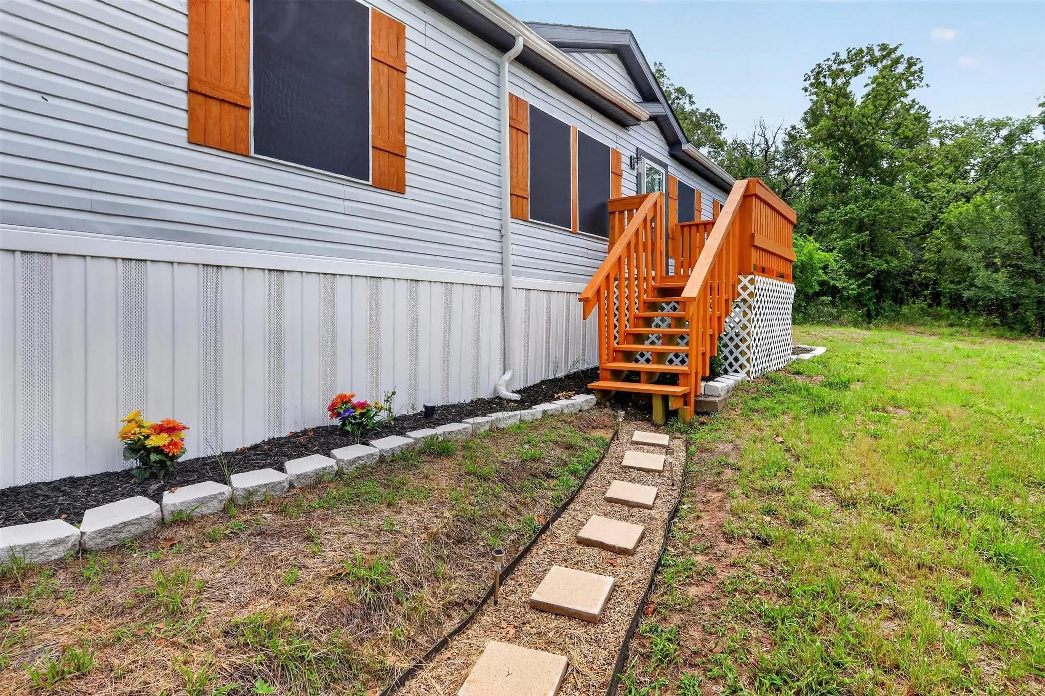 Exterior featuring light gray siding, wood-toned shutters, and a matching wood-toned entrance staircase with railing