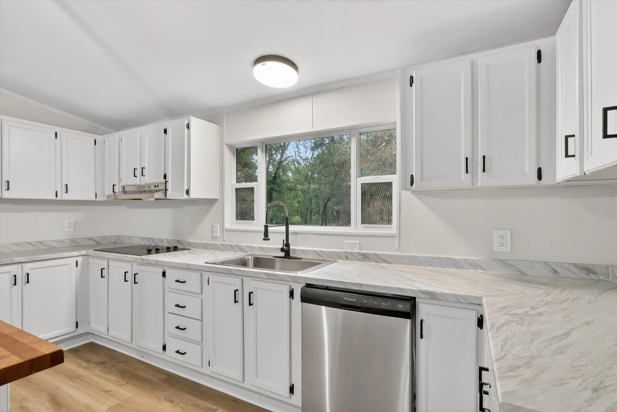 Open-concept kitchen featuring white cabinetry, light-toned wood-finish flooring, and a central island with a wood countertop