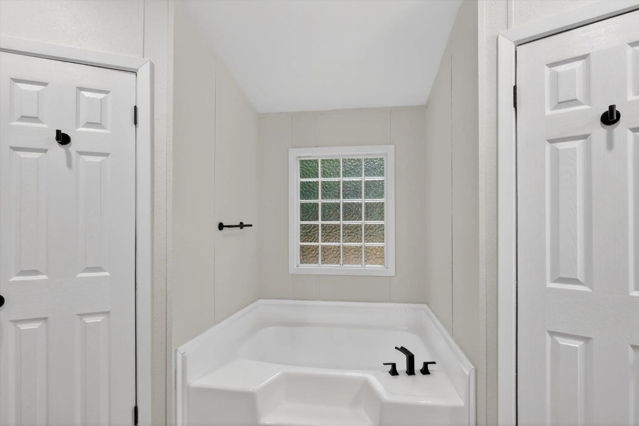 White soaking tub with matte black fixtures, framed by light-colored panel walls