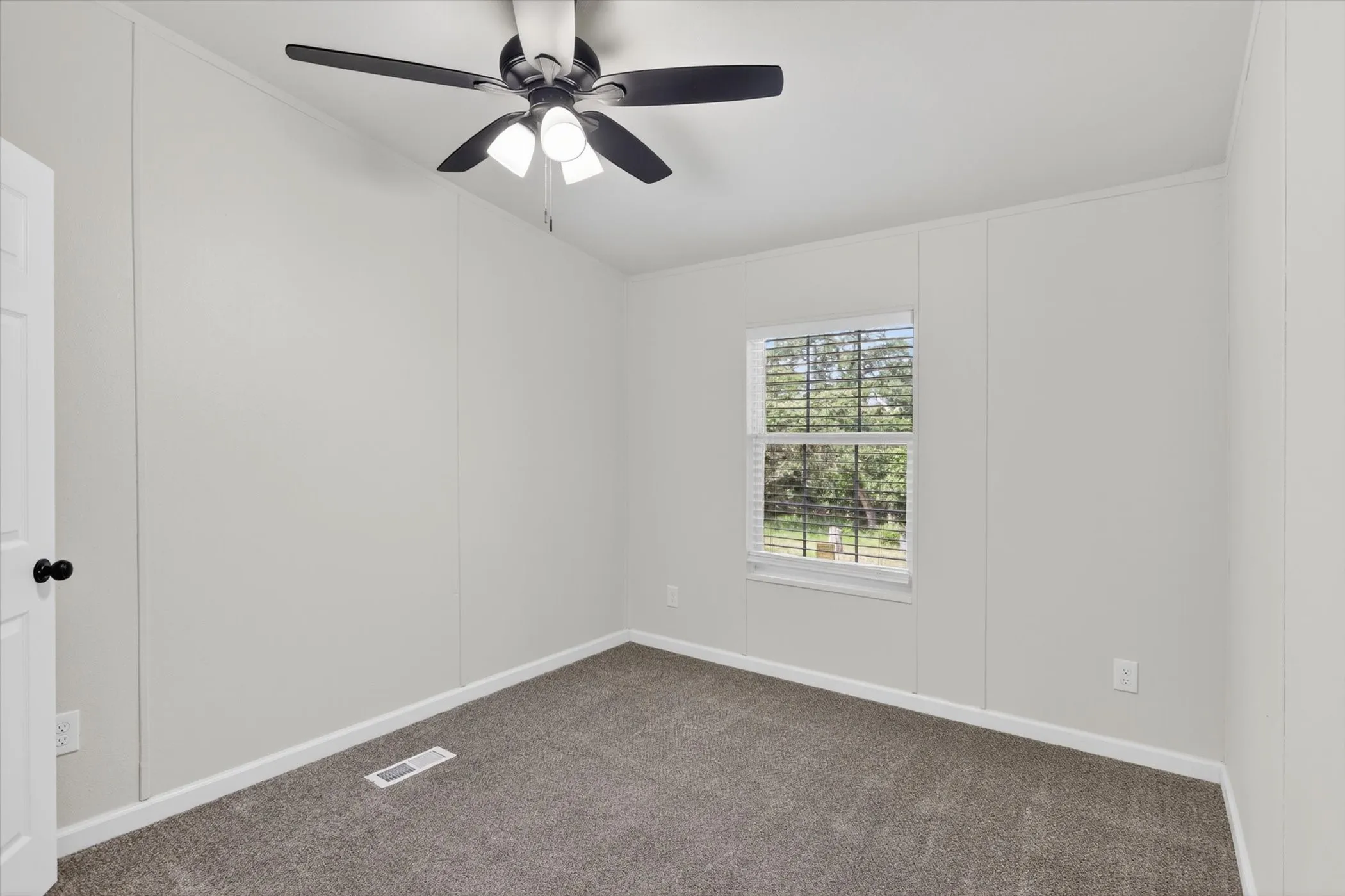 Carpeted room with a ceiling fan featuring integrated lighting, a single window with blinds, and white trim molding