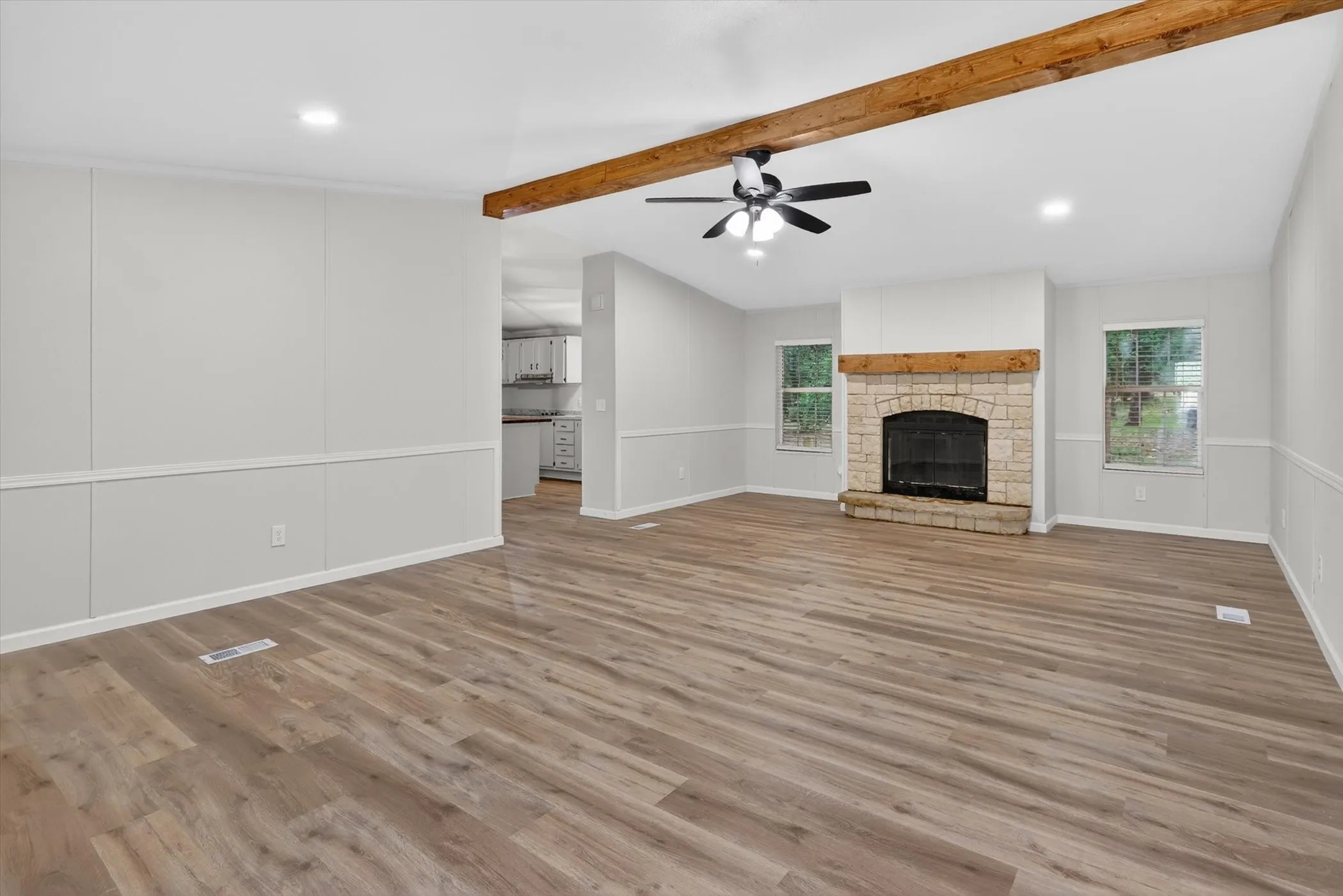 Spacious interior featuring wood-finish flooring, a stone fireplace with a wood mantle, and exposed ceiling beams