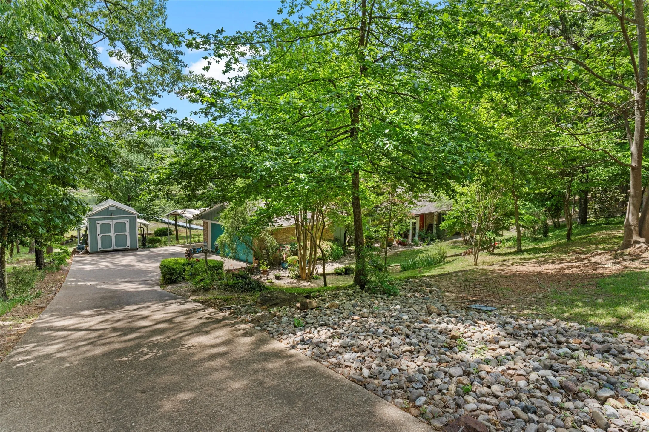 Paved driveway leading to a detached shed with double doors and a covered carport