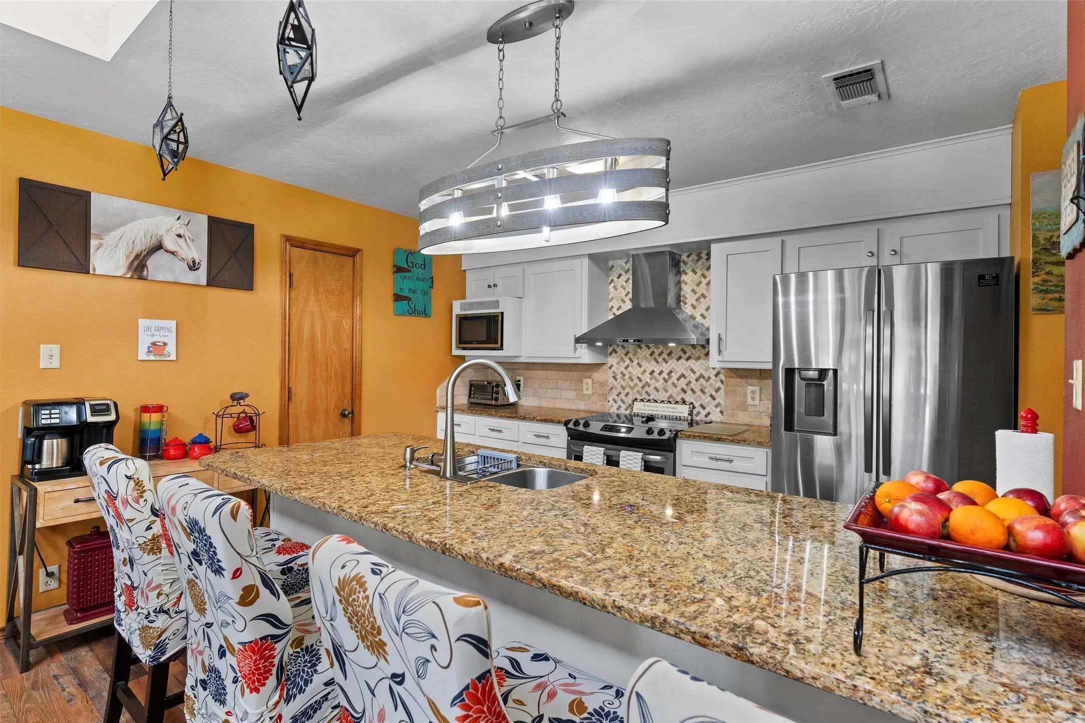 Spacious kitchen featuring a large island with a stone-finish countertop, stainless steel appliances, light-toned cabinetry, and a patterned tile backsplash