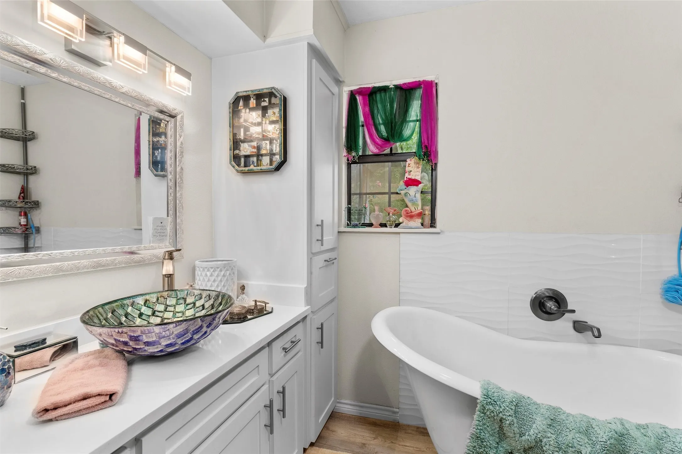 Bathroom featuring a freestanding tub, mosaic vessel sink, white vanity with ample storage, and wood-finish flooring