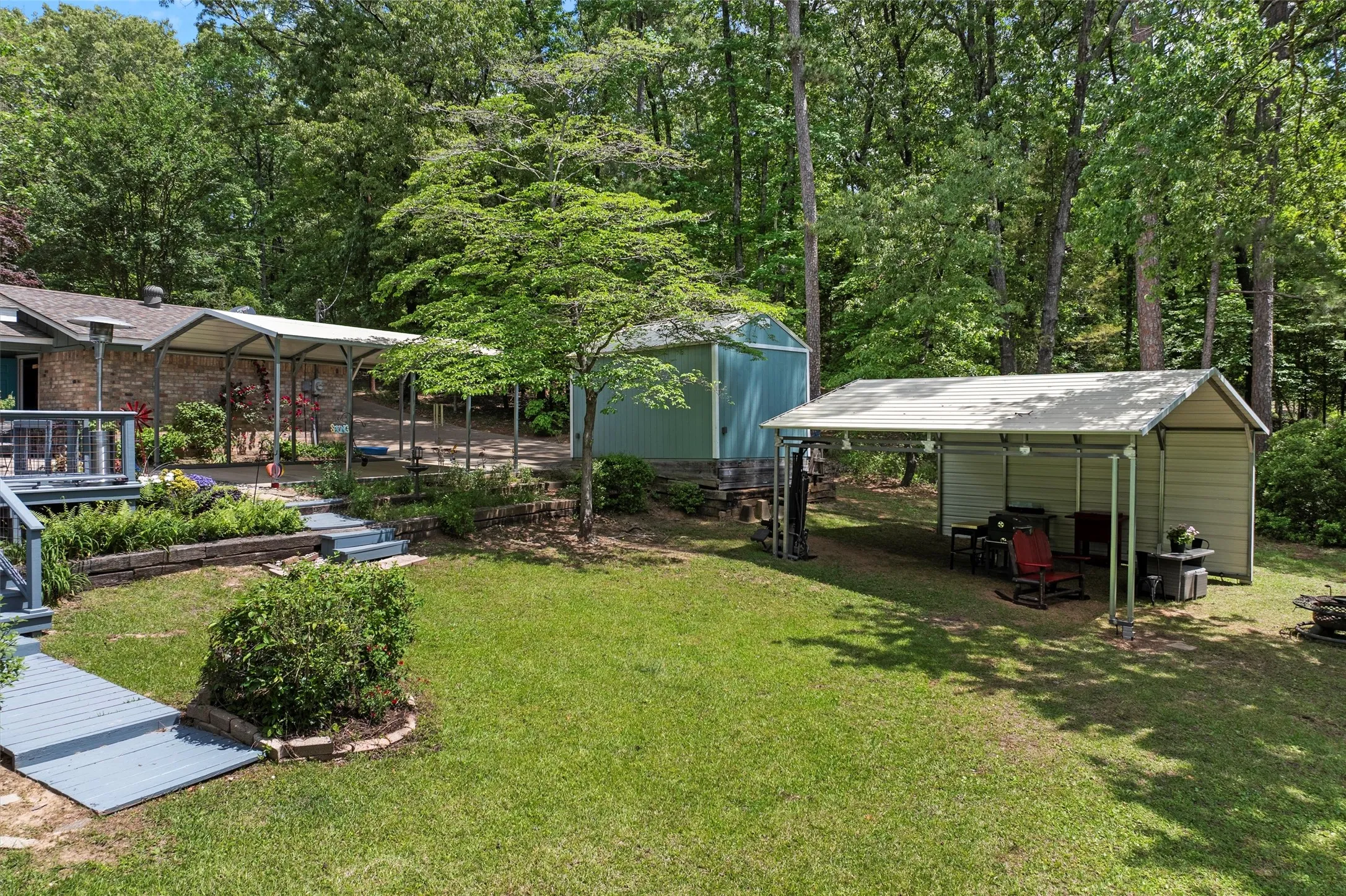 Expansive backyard featuring a lush lawn, multiple covered outdoor structures, a detached storage shed, and mature trees providing a natural backdrop