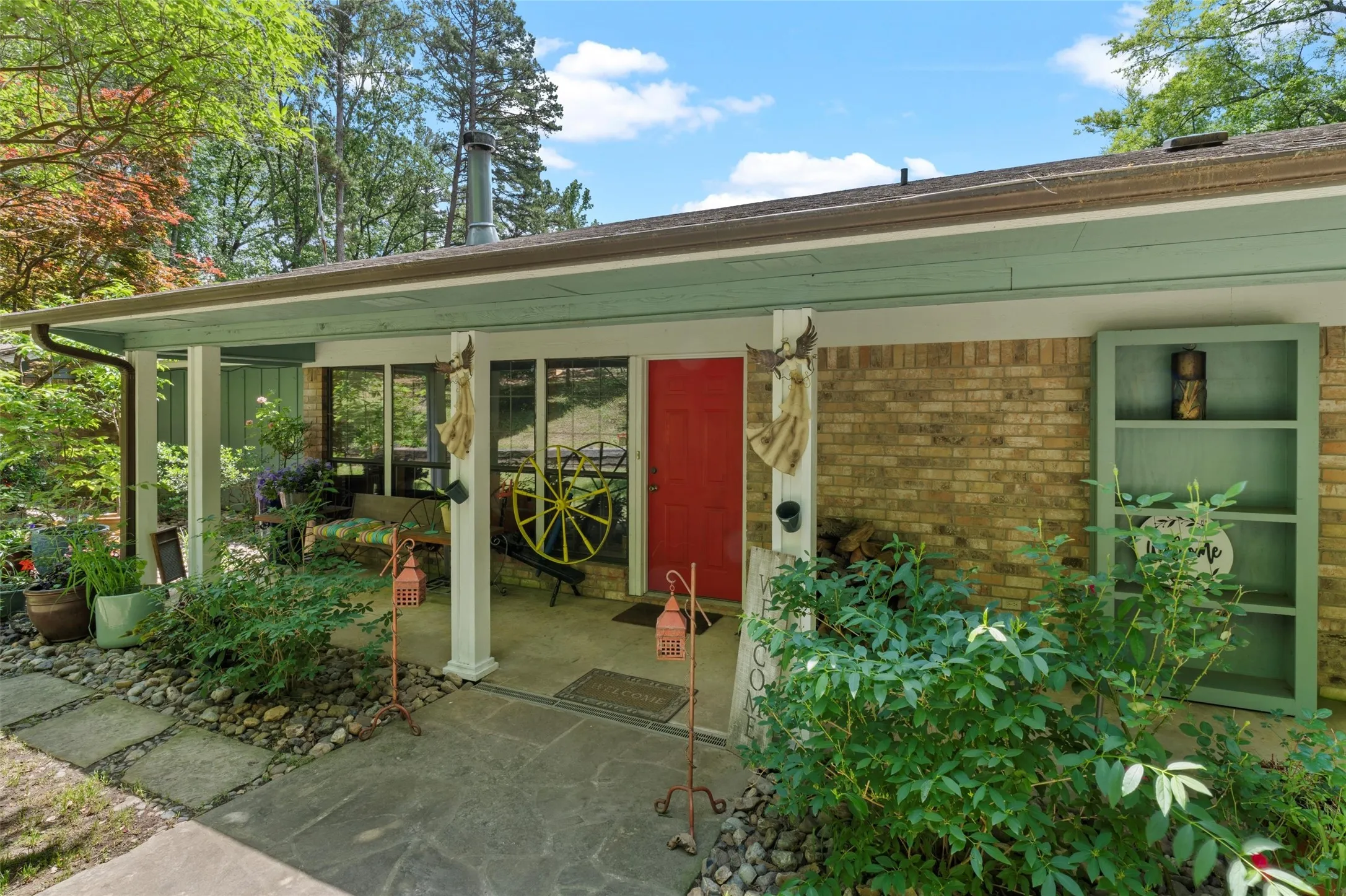 Brick exterior featuring a covered porch, a vibrant red entry door, an integrated green bookcase, and a stone paver walkway