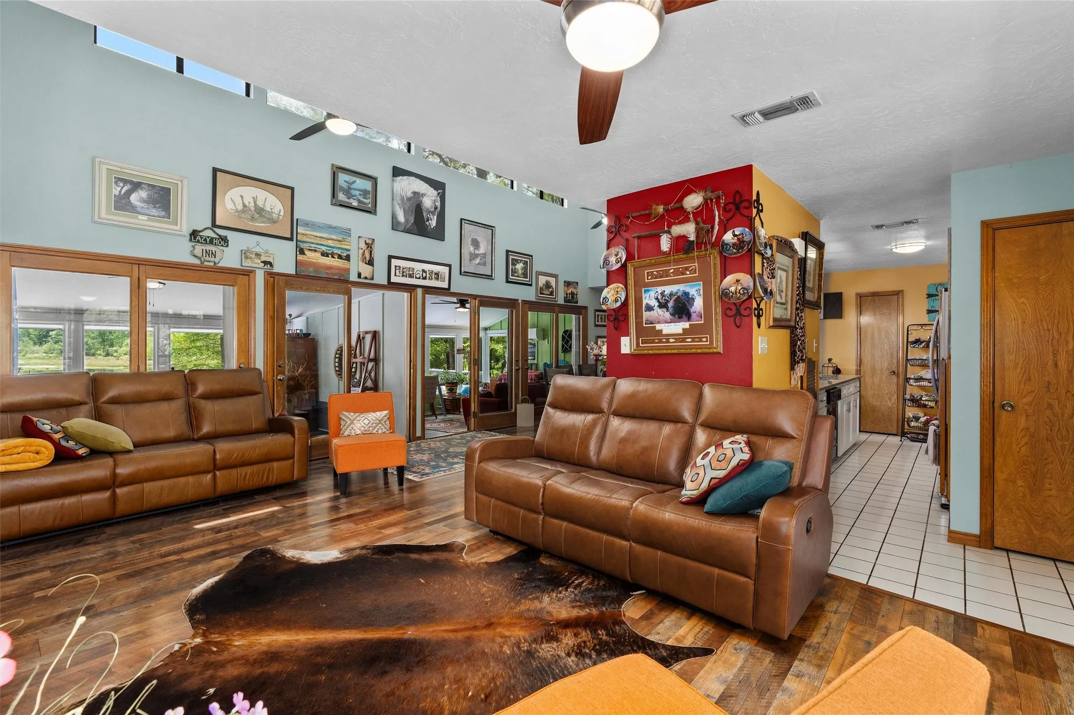 Spacious living area featuring wood-finish flooring, a vaulted ceiling with a fan, and large windows with transom lighting
