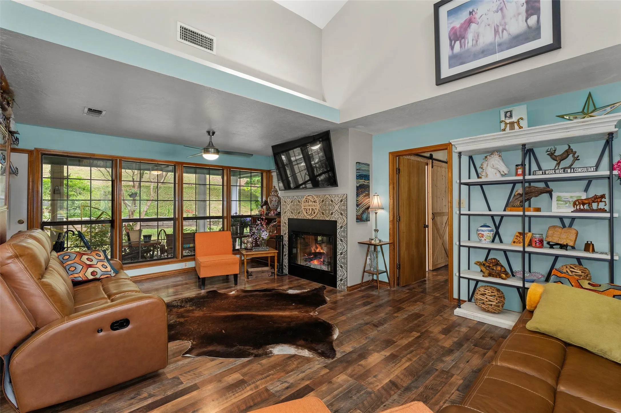 Living area featuring wood-finish flooring, a decorative tile fireplace surround, vaulted ceilings, and a built-in shelving unit