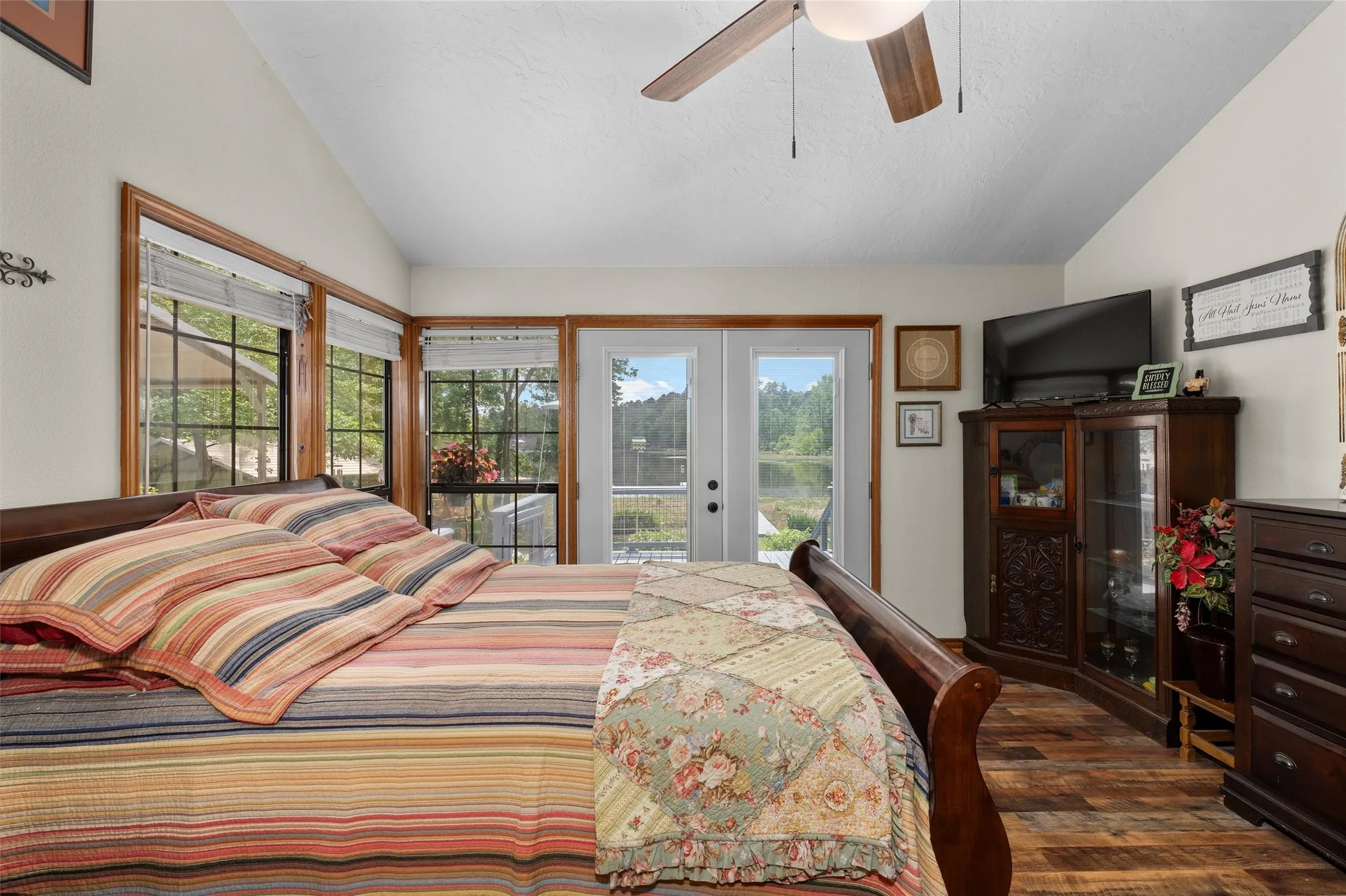 Vaulted ceilings with a ceiling fan, French doors, wood-finish flooring, and multiple windows with wood trim