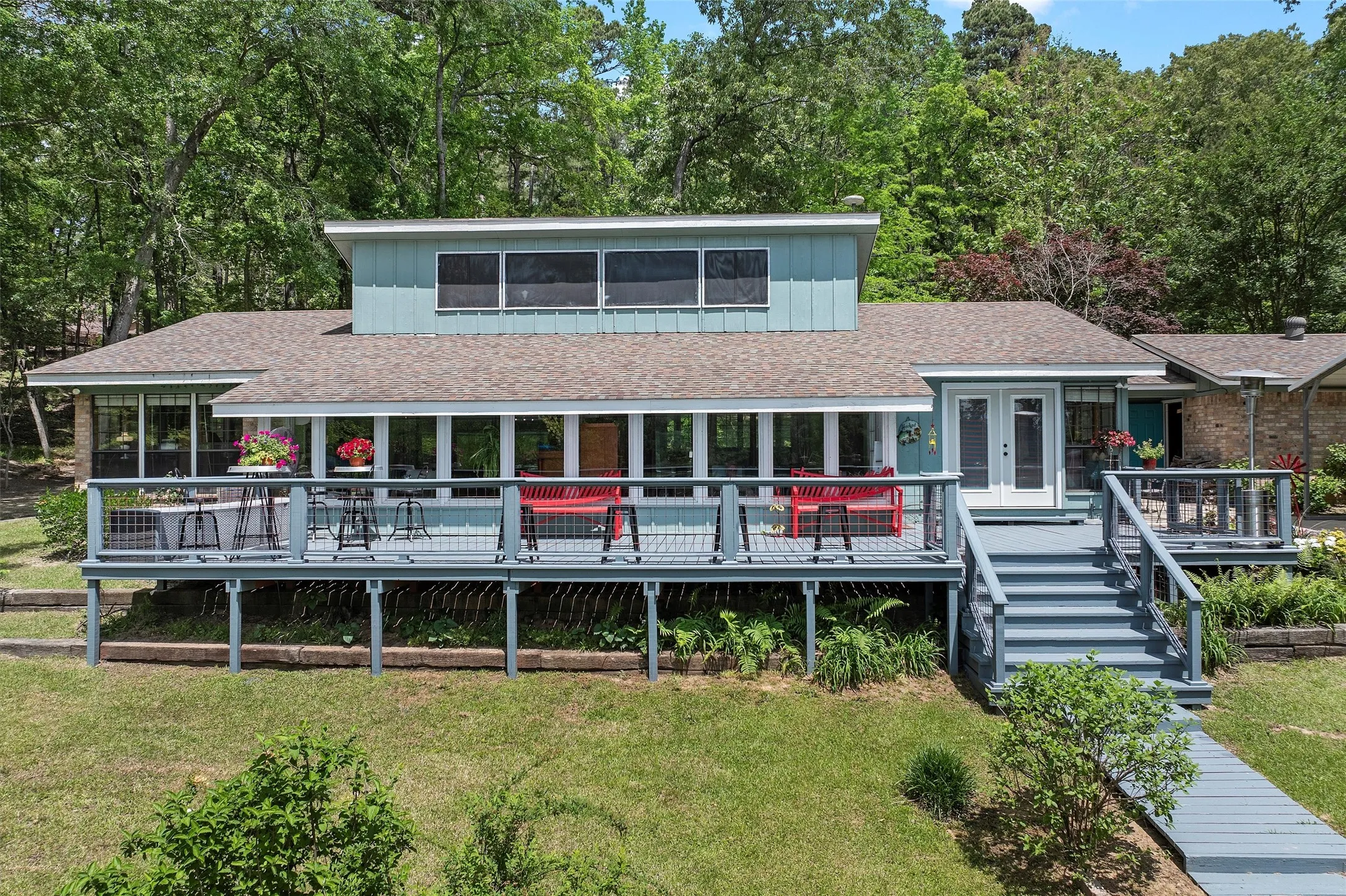 Elevated residence featuring a broad deck with railing, a multi-paneled sunroom, and a second-story dormer with multiple windows
